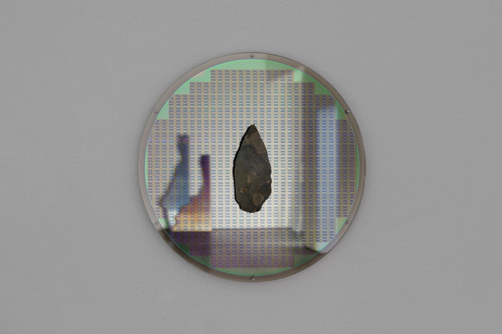 Anima Atman by Troika at Max Goelitz — A dark, teardrop-shaped stone artifact is suspended within a circular acrylic frame mounted on a gallery wall.