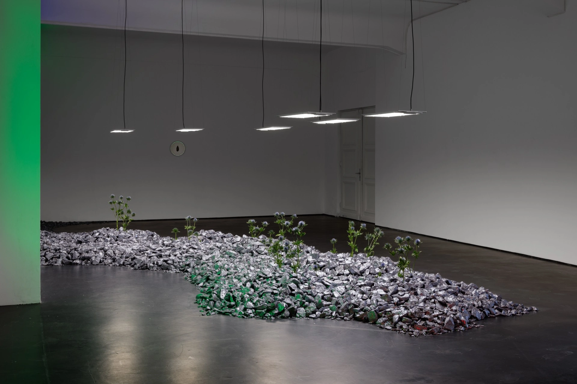 Anima Atman by Troika at Max Goelitz — A gallery installation featuring a crushed stone and mineral aggregate bed in pale grey, scattered across dark flooring in an asymmetric configuration.