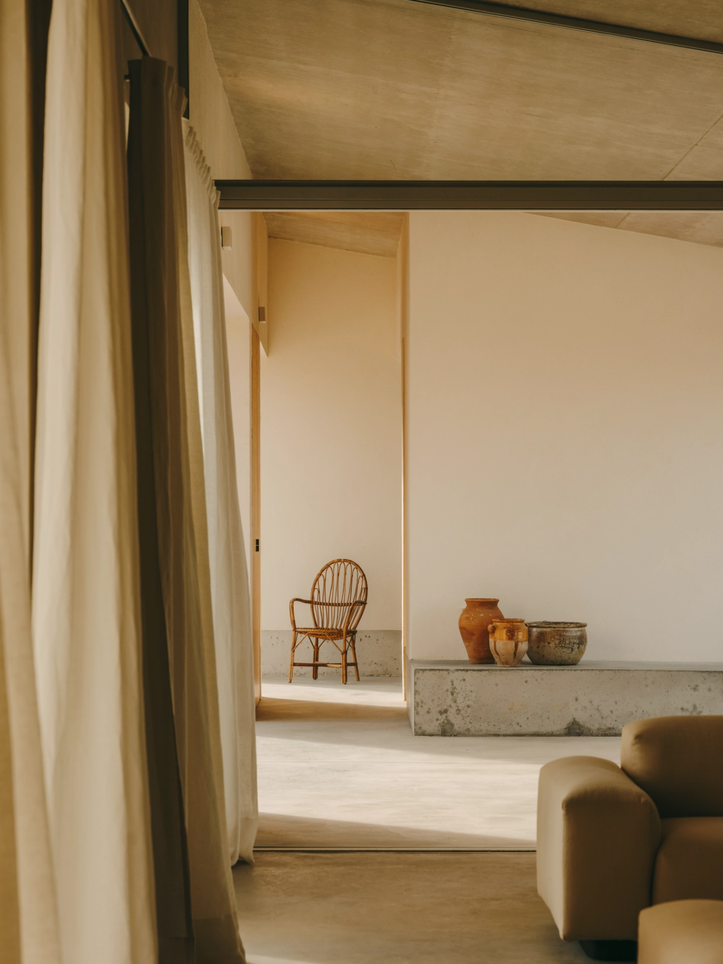 Casa TD by Skye Maunsell, Jordi Veciana and Juan Gurrea Rumeu — A threshold view into a minimalist interior spatial sequence, where a cream linen curtain suspended from ceiling creates soft division between rooms.