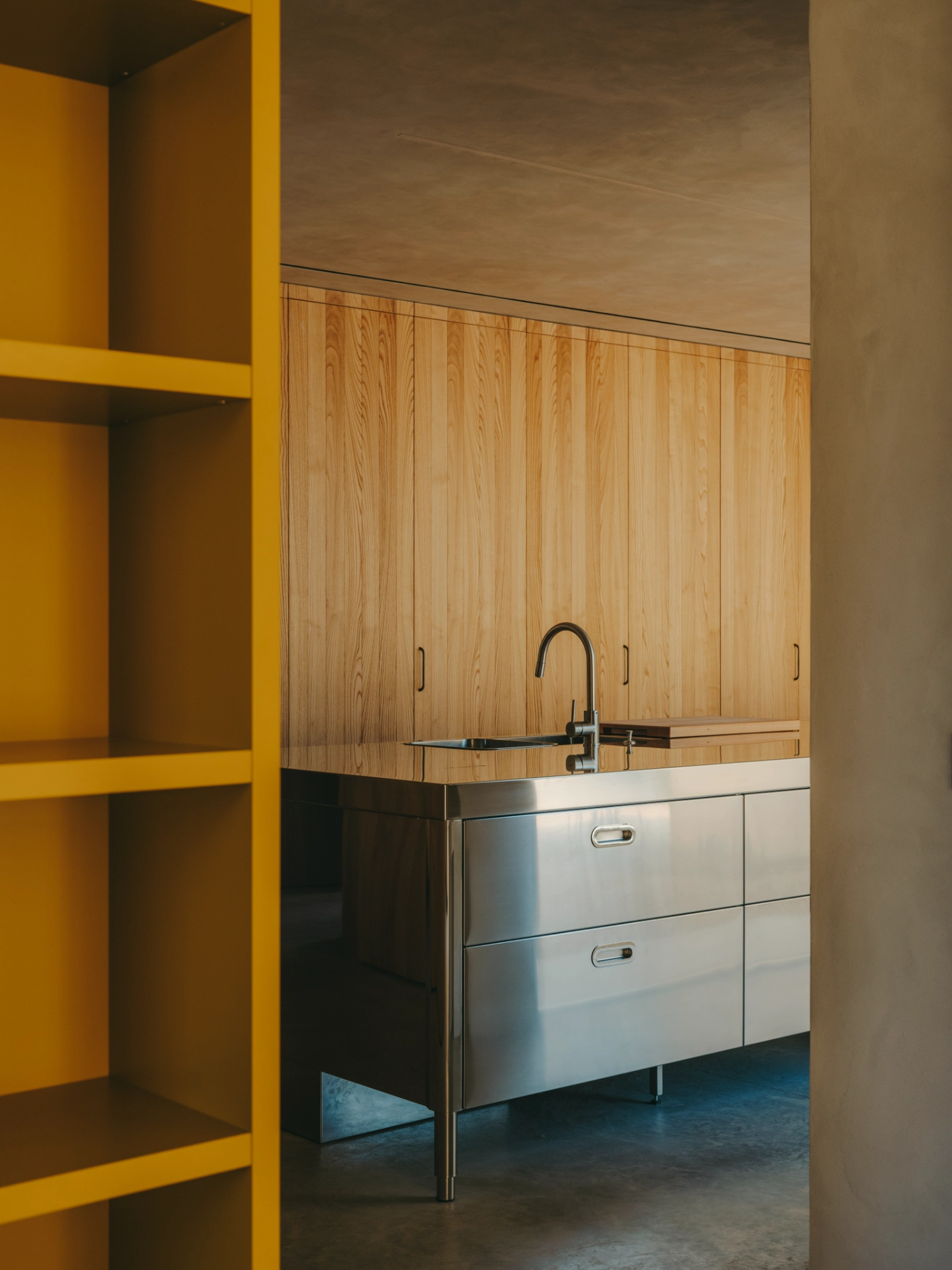 Casa TD by Skye Maunsell, Jordi Veciana and Juan Gurrea Rumeu — A kitchen alcove anchored by a stainless steel sink unit with two deep drawers, positioned beneath vertical timber cabinetry with wood-grain detailing.