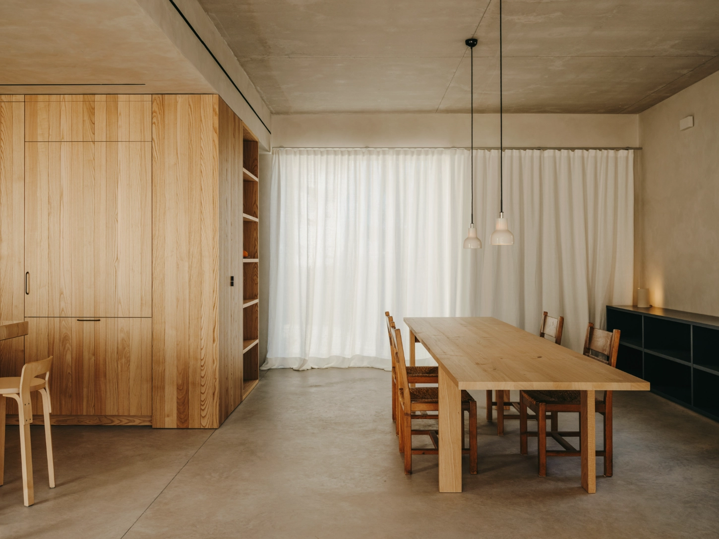 Casa TD by Skye Maunsell, Jordi Veciana and Juan Gurrea Rumeu — The dining volume frames a threshold between interior and courtyard, anchored by a timber table with rush-seated chairs positioned to capture the stone...