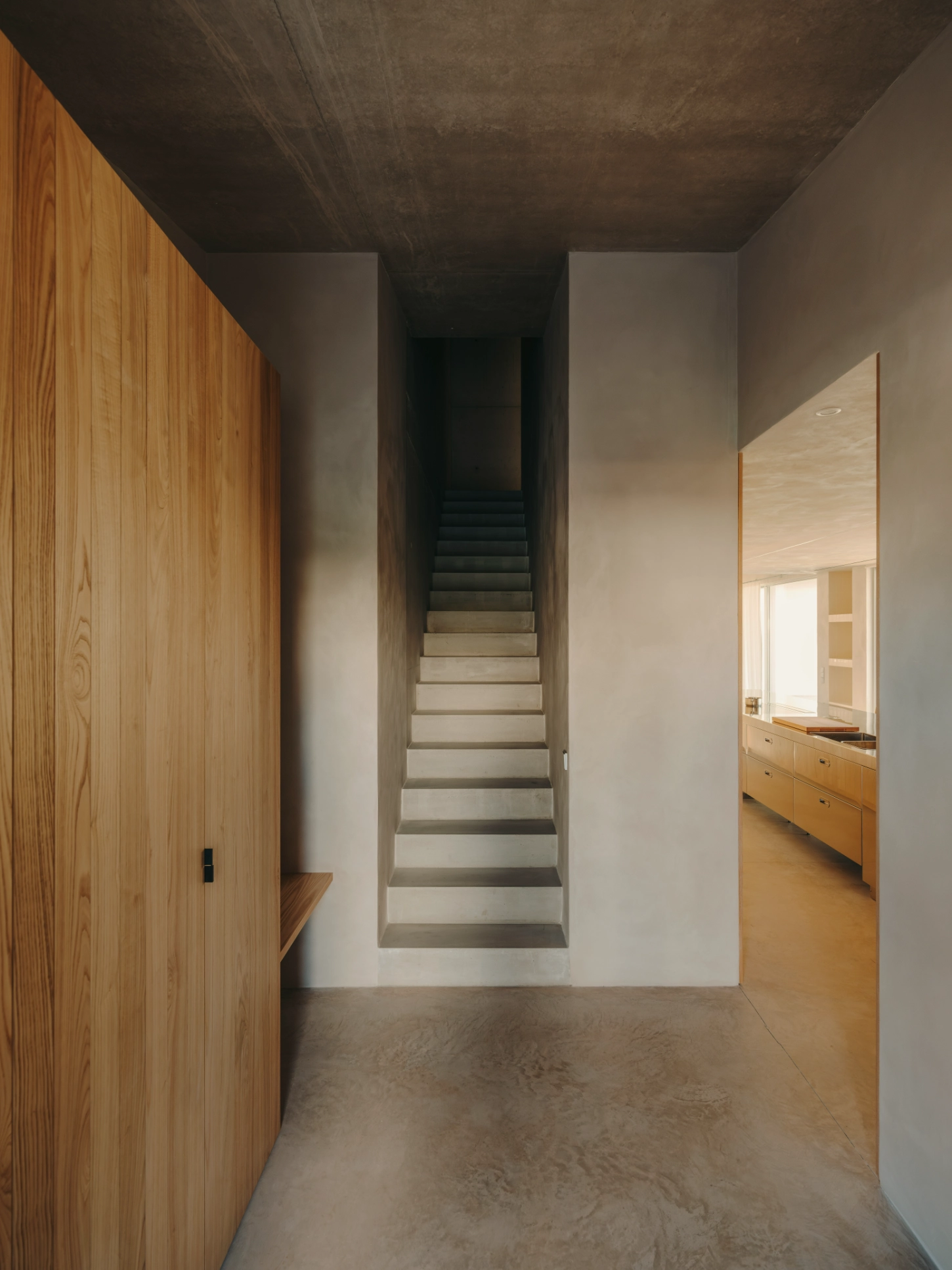 Casa TD by Skye Maunsell, Jordi Veciana and Juan Gurrea Rumeu — A narrow corridor anchors the spatial progression through Casa TD, framed by a timber-clad wall on the left and rendered surfaces on the right.