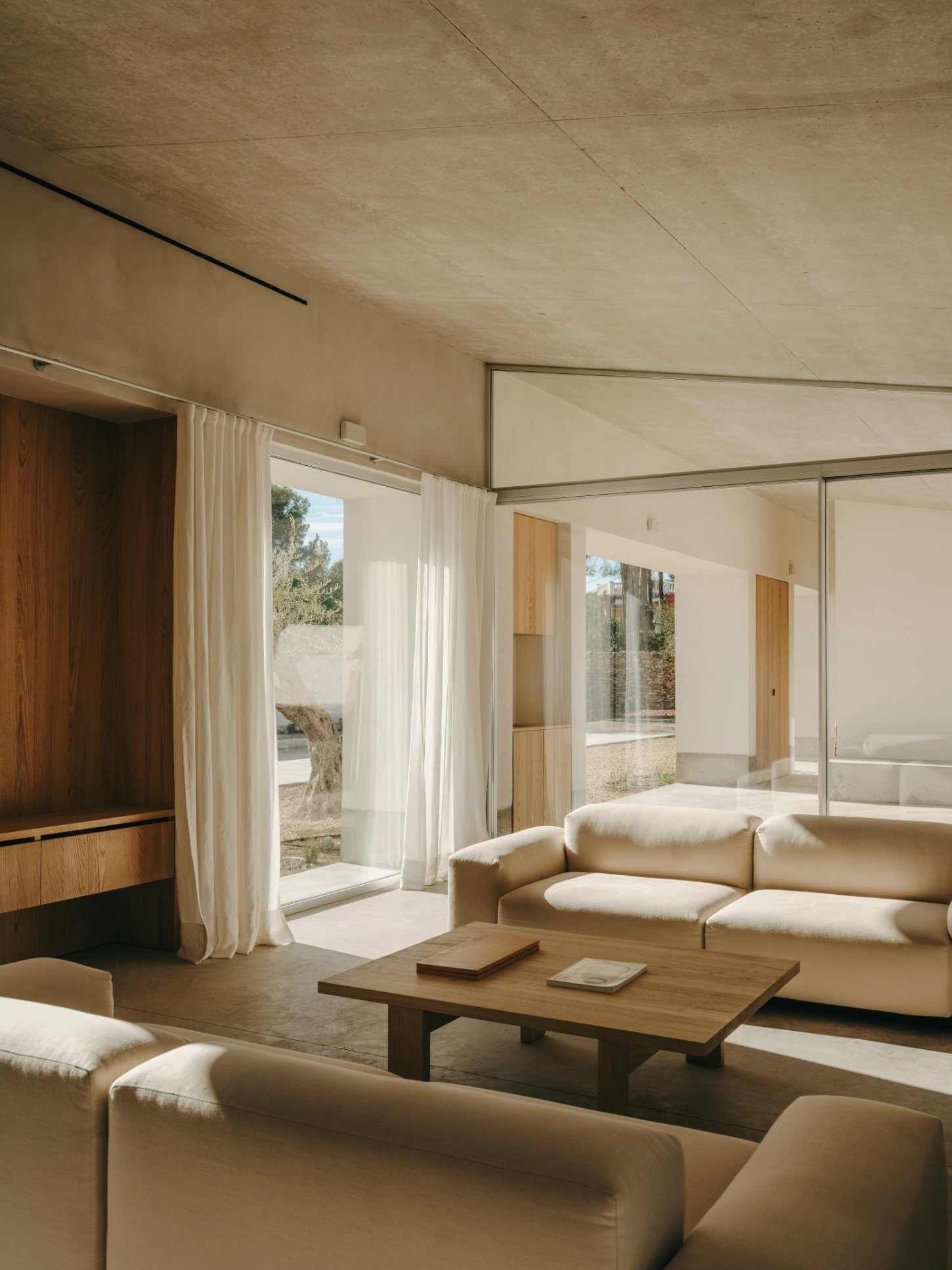 Casa TD by Skye Maunsell, Jordi Veciana and Juan Gurrea Rumeu — The living room presents a layered spatial composition anchored by a low timber table positioned to frame the courtyard view beyond.