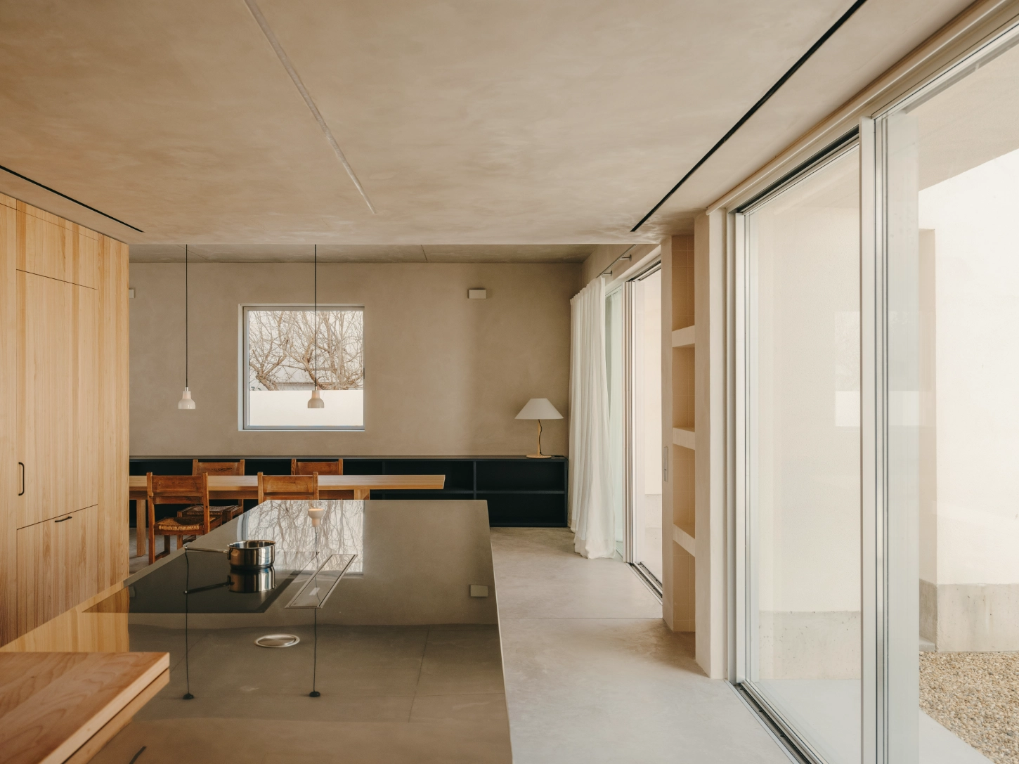 Casa TD by Skye Maunsell, Jordi Veciana and Juan Gurrea Rumeu — The open-plan interior frames a precisely composed view toward the courtyard olive tree through a timber-framed window.