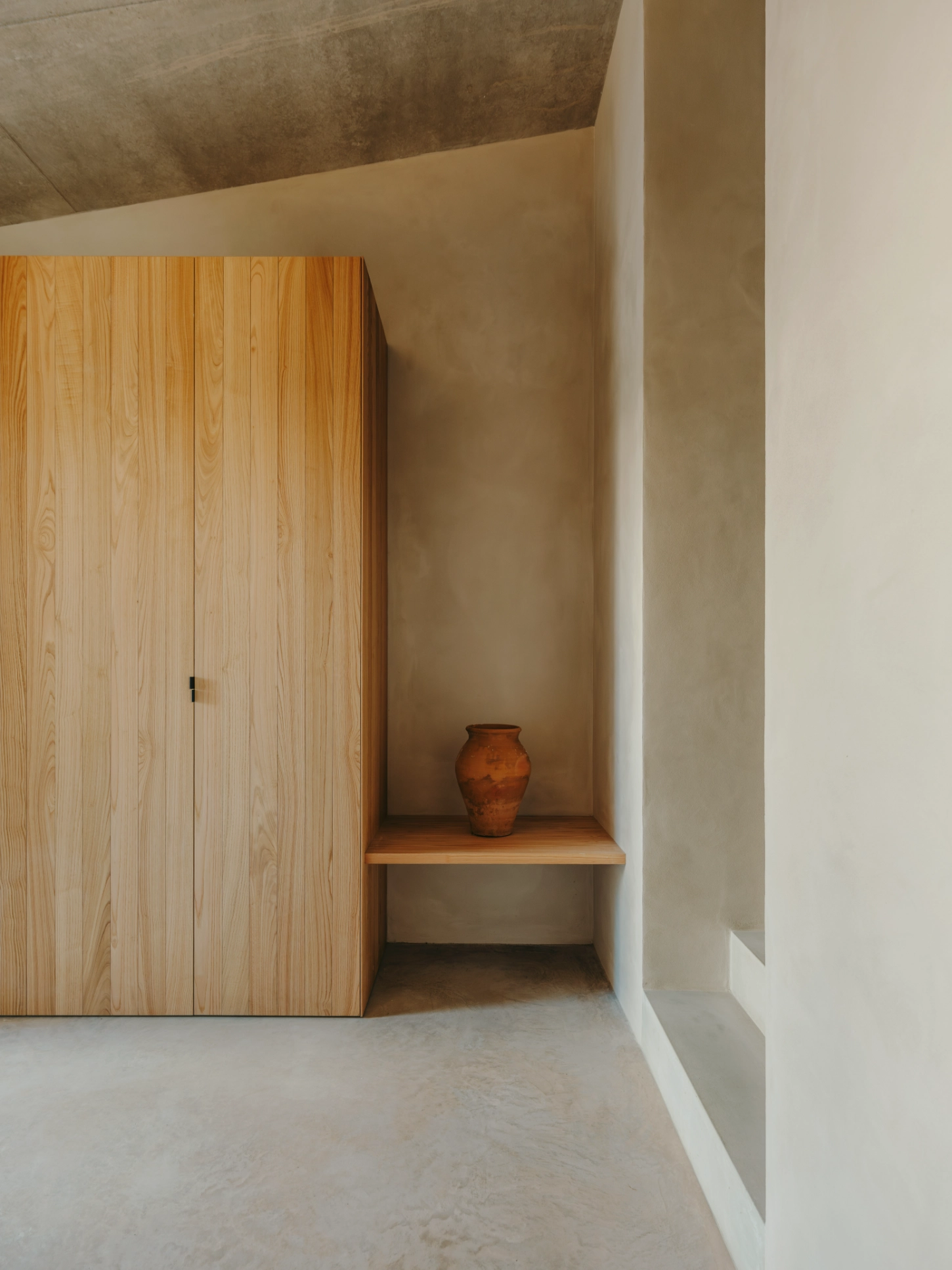 Casa TD by Skye Maunsell, Jordi Veciana and Juan Gurrea Rumeu — A recessed alcove punctuates the cream-rendered wall, its depth emphasized by a wooden shelf that interrupts the vertical plane.