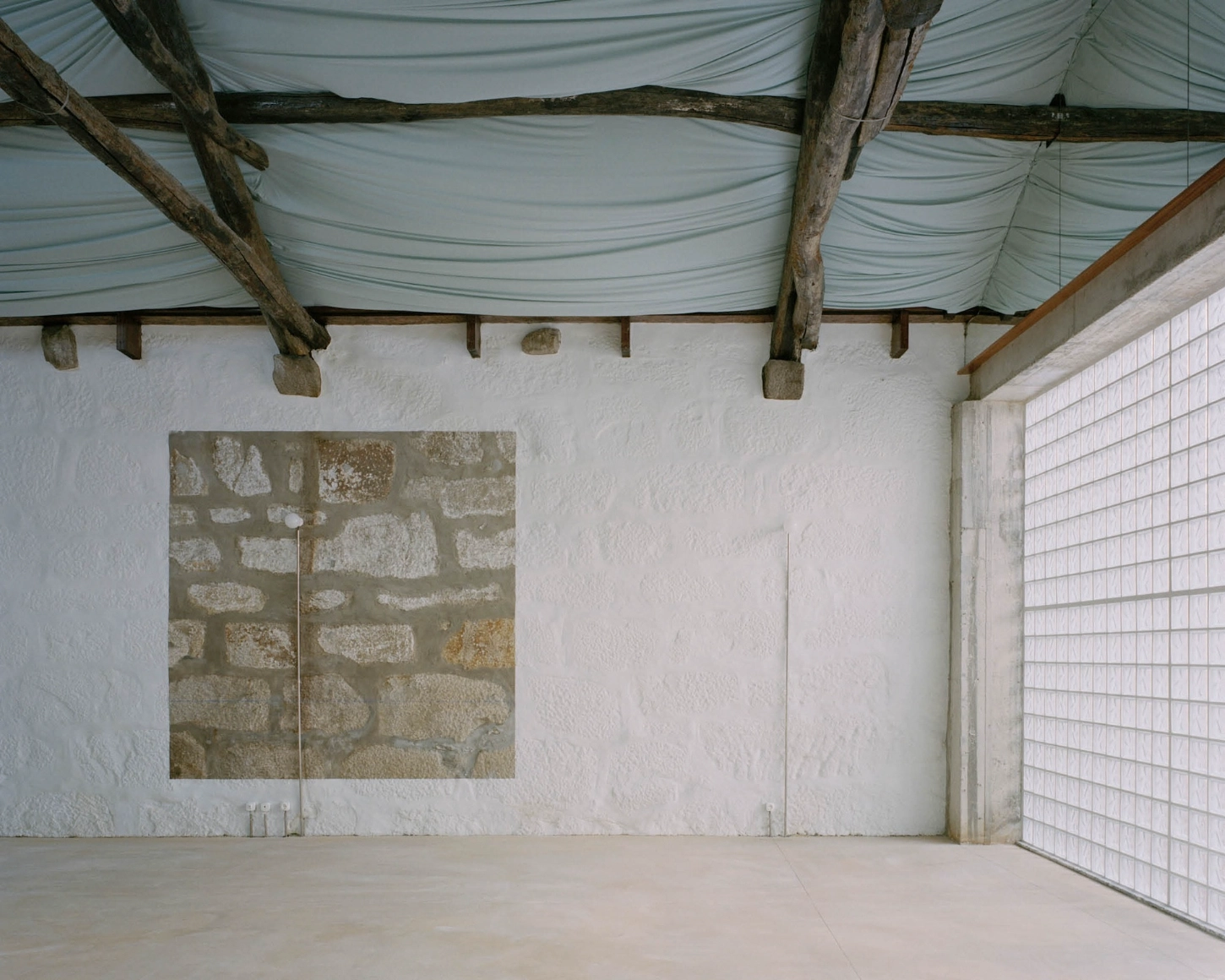 'House with many faces' by Fala Atelier — A post-and-beam interior with exposed timber roof structure supporting corrugated metal sheeting, the beams exhibiting weathered patina.