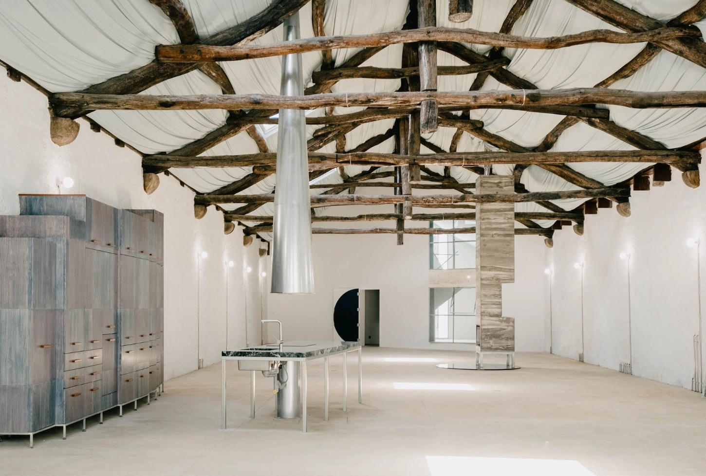 'House with many faces' by Fala Atelier — A renovated industrial space with exposed timber roof structure, where weathered wooden beams and corrugated metal sheeting create a geometric lattice overhead.