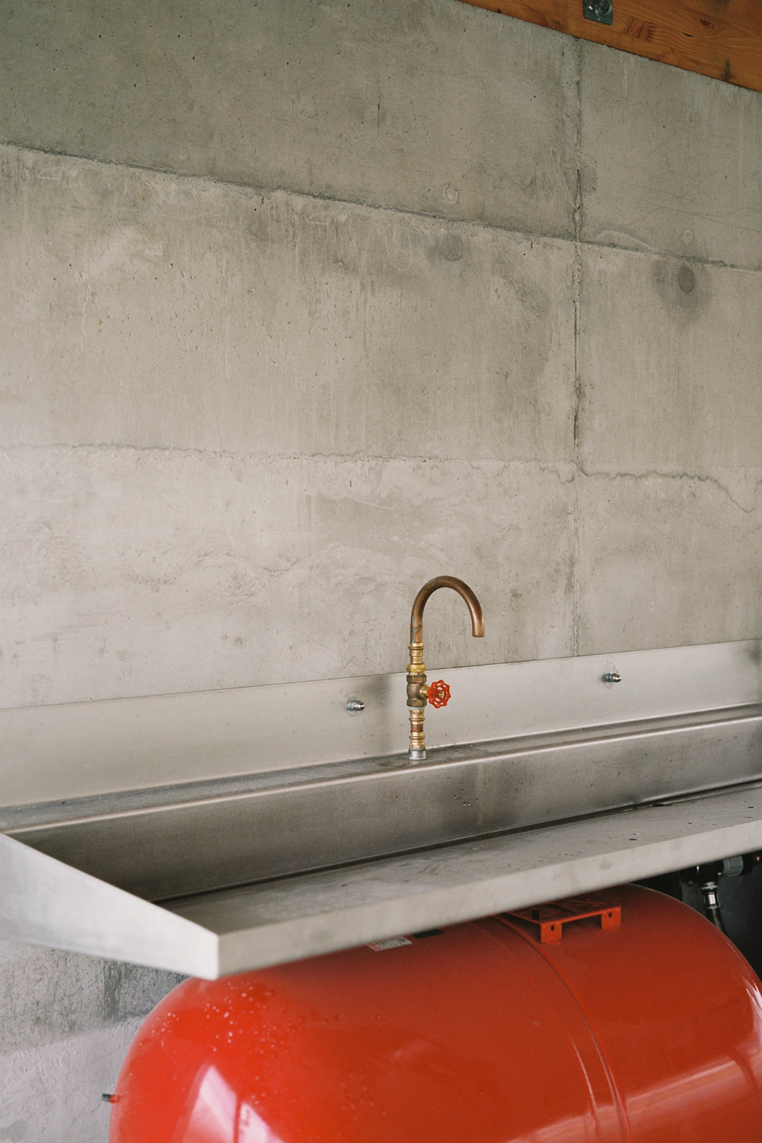 Garden Pavilion by Esnard Sanz Architectes — A utility sink detail captured mid-construction, featuring a brass-patinated gooseneck tap with red ball valve mounted on a stainless steel counter.
