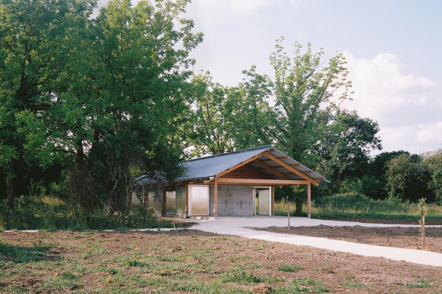 Garden Pavilion by Esnard Sanz Architectes — A timber-framed pavilion with gabled roof sits within a grove of mature deciduous trees in Villenave-d'Ornon.