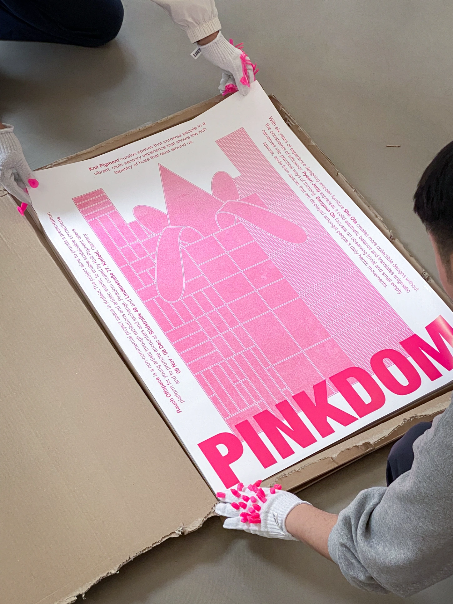 PINKDOM by Knit Pigment — Documentation photograph from PINKDOM exhibition showing a knit pigment sample card held by gloved hands in white socks.
