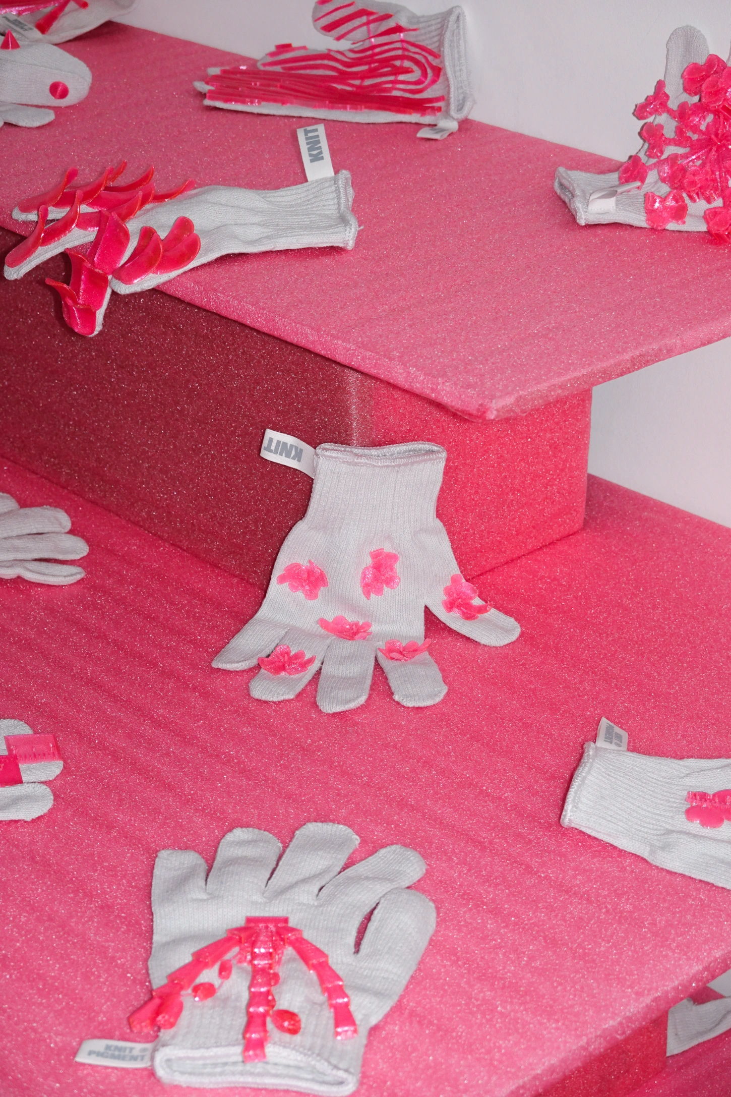 PINKDOM by Knit Pigment — White ribbed gloves with hot pink embroidered or appliqué maple leaf motifs arranged across a vivid hot pink textured background.