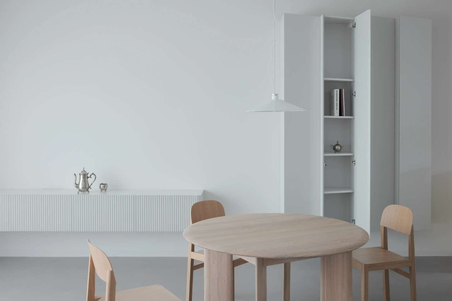 VVV by i.B Archstudio — A light wood dining table with organic curved edges anchors the minimalist interior, surrounded by bentwood chairs with cream-colored seats.