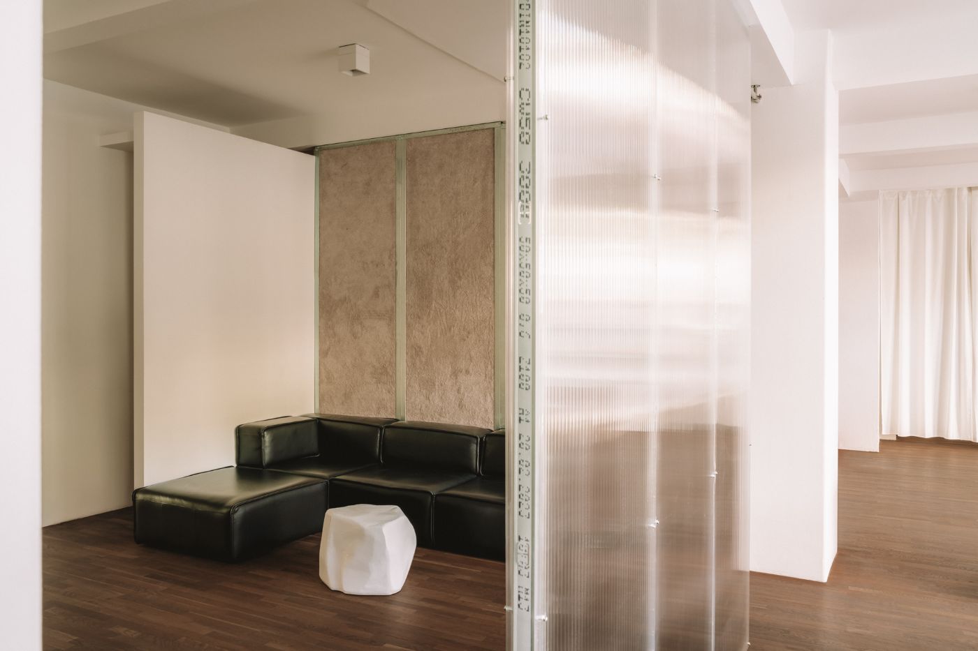 KMB Torstrasse 140 by Vaust — A sectioned interior workspace featuring a black leather modular seating unit positioned beneath suspended timber and plaster acoustic panels.