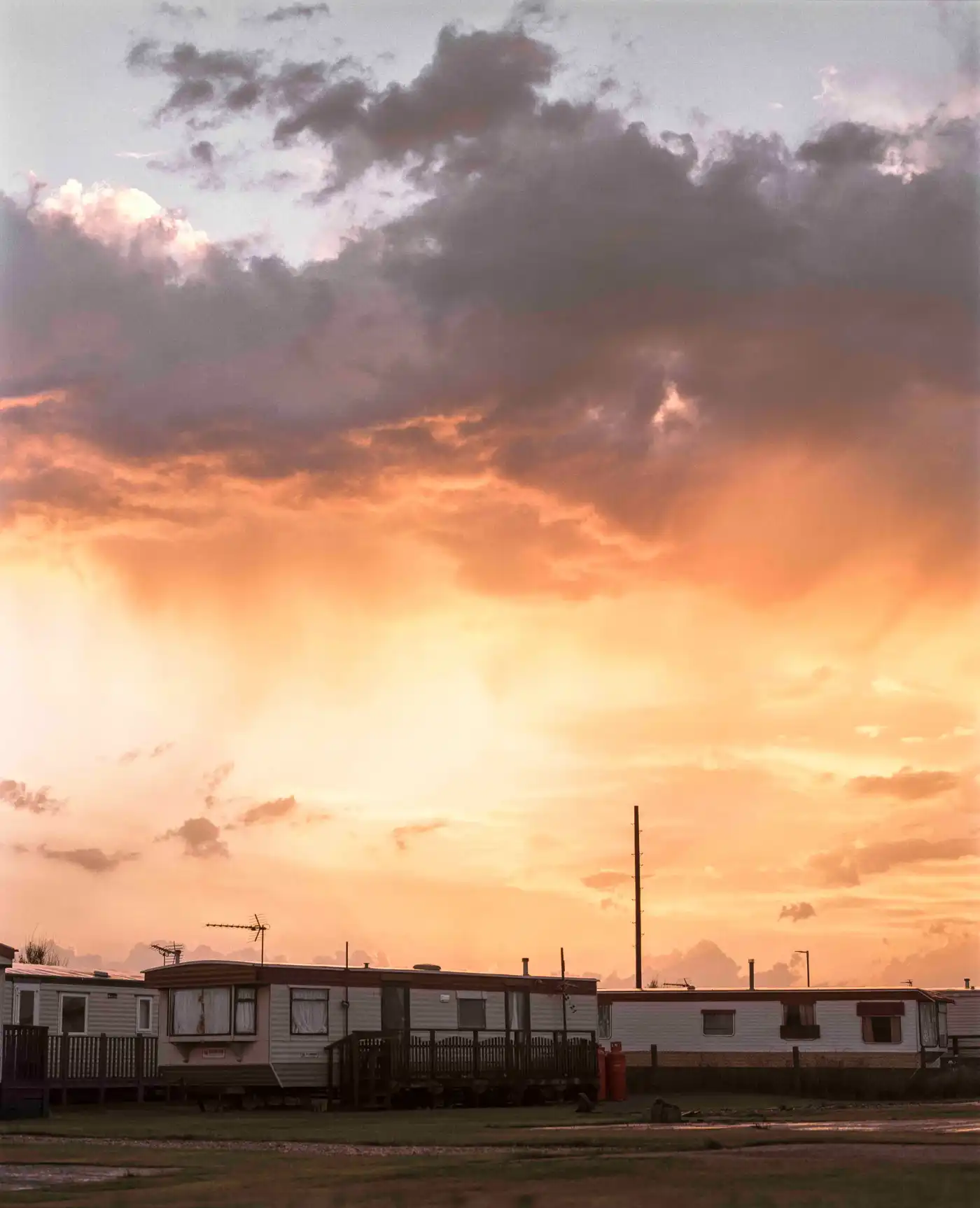 Land Loss by Max Miechowski — A row of residential mobile homes sits silhouetted against a dramatic sunset sky in horizontal composition.