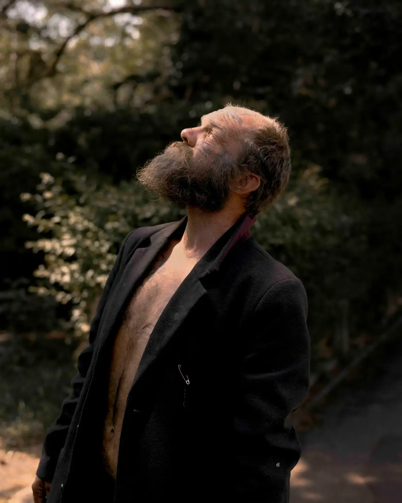 Land Loss by Max Miechowski — A man with grey beard and receding hairline stands in profile against flowering shrubs, head tilted back in an upward gaze.