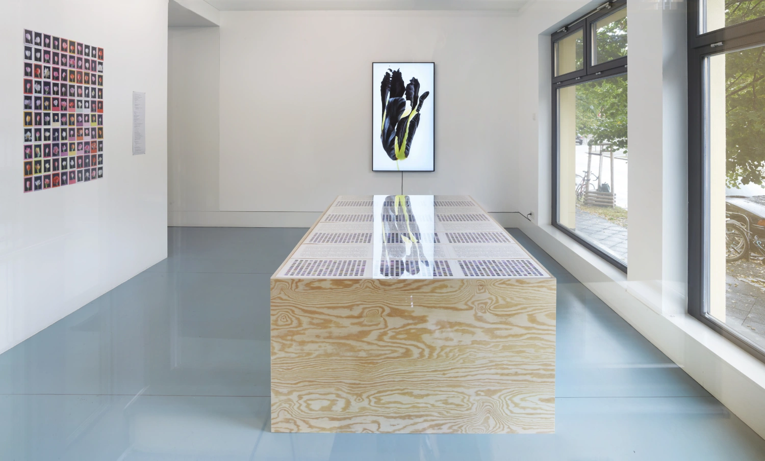 Time Within Time by Anna Ridler at Crypto Kiosk — A linear wooden display table runs the length of a bright corridor, its plywood surface perforated with a gridded pattern of small apertures.