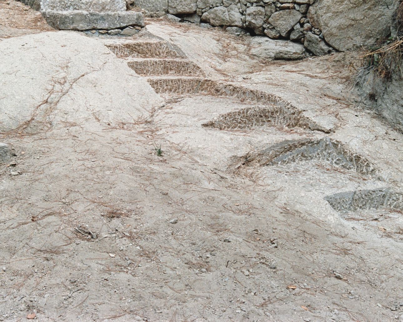House in Ancede by atelier local — Ground-level view of an unfinished concrete floor slab bordered by stone masonry walls.