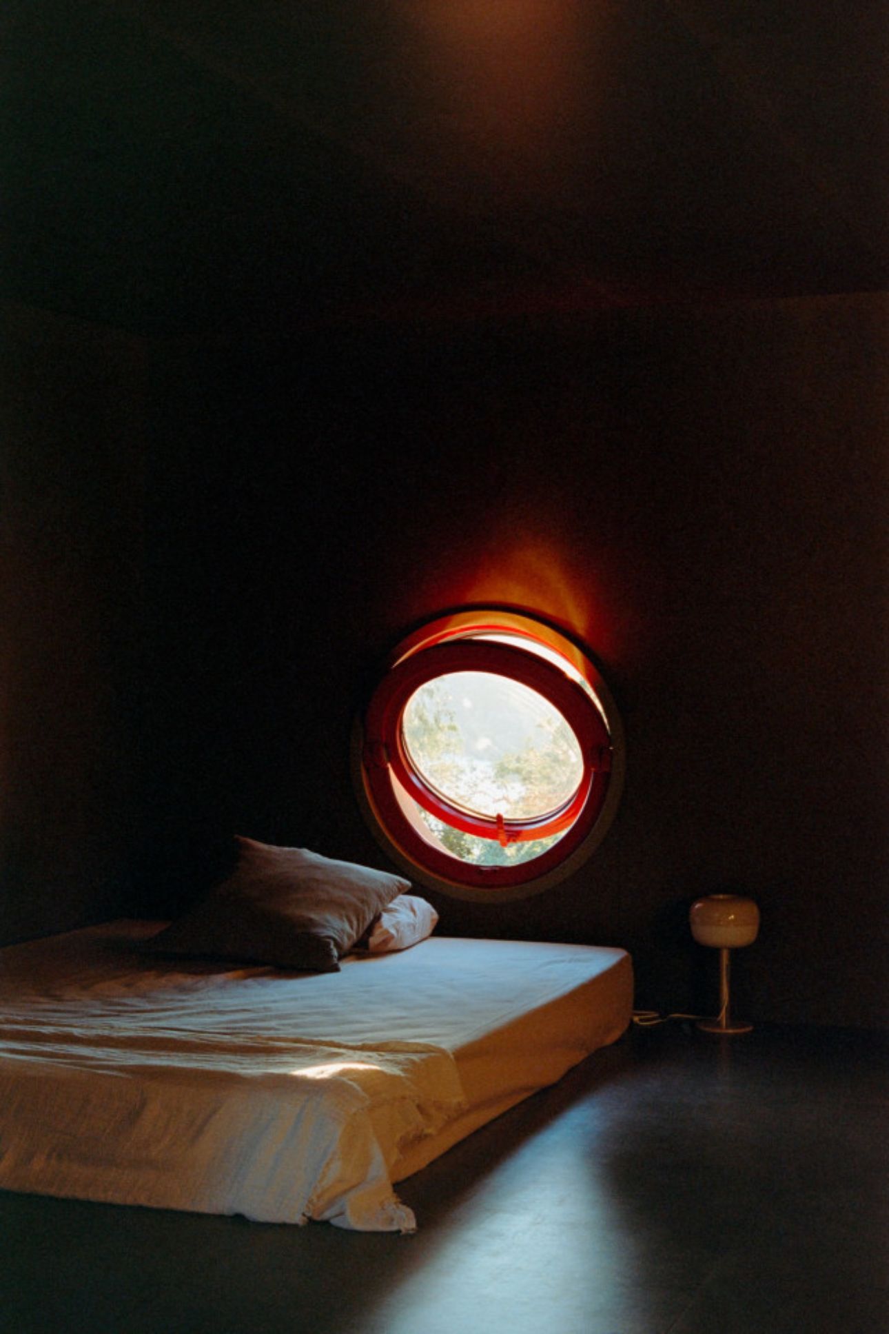House in Ancede by atelier local — A circular red-framed porthole window dominates the composition, its warm glow creating a halo effect against the dark interior.