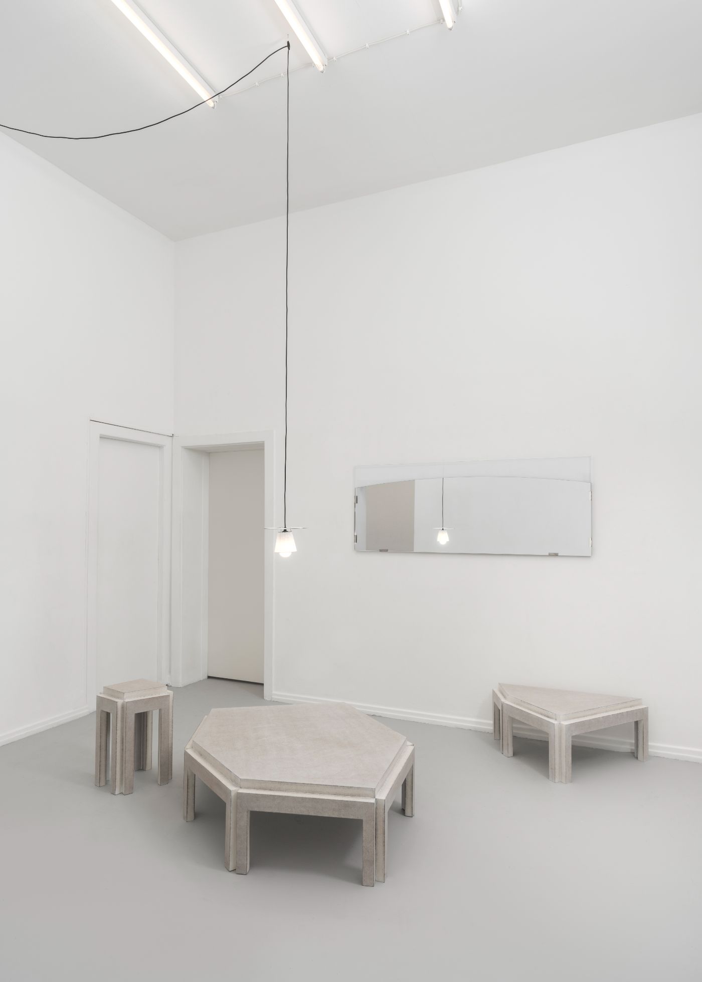 Selected Works by Bahraini-Danish — A minimalist interior space features a geometric table with an undulating, octagonal tabletop in light timber, supported by two curved legs with organic...