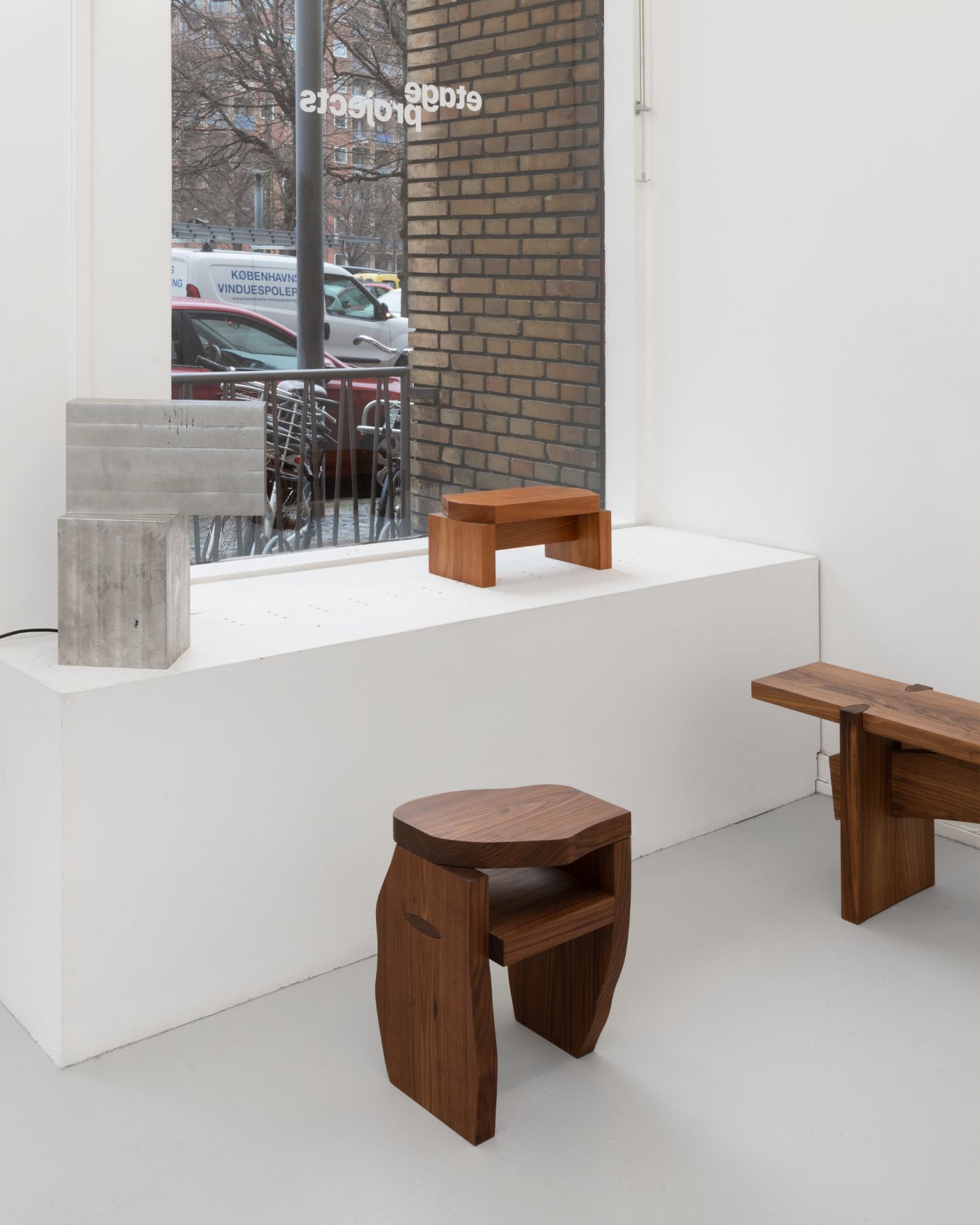 Selected Works by Bahraini-Danish — A minimalist interior display featuring three wooden furniture pieces arranged on a white platform.