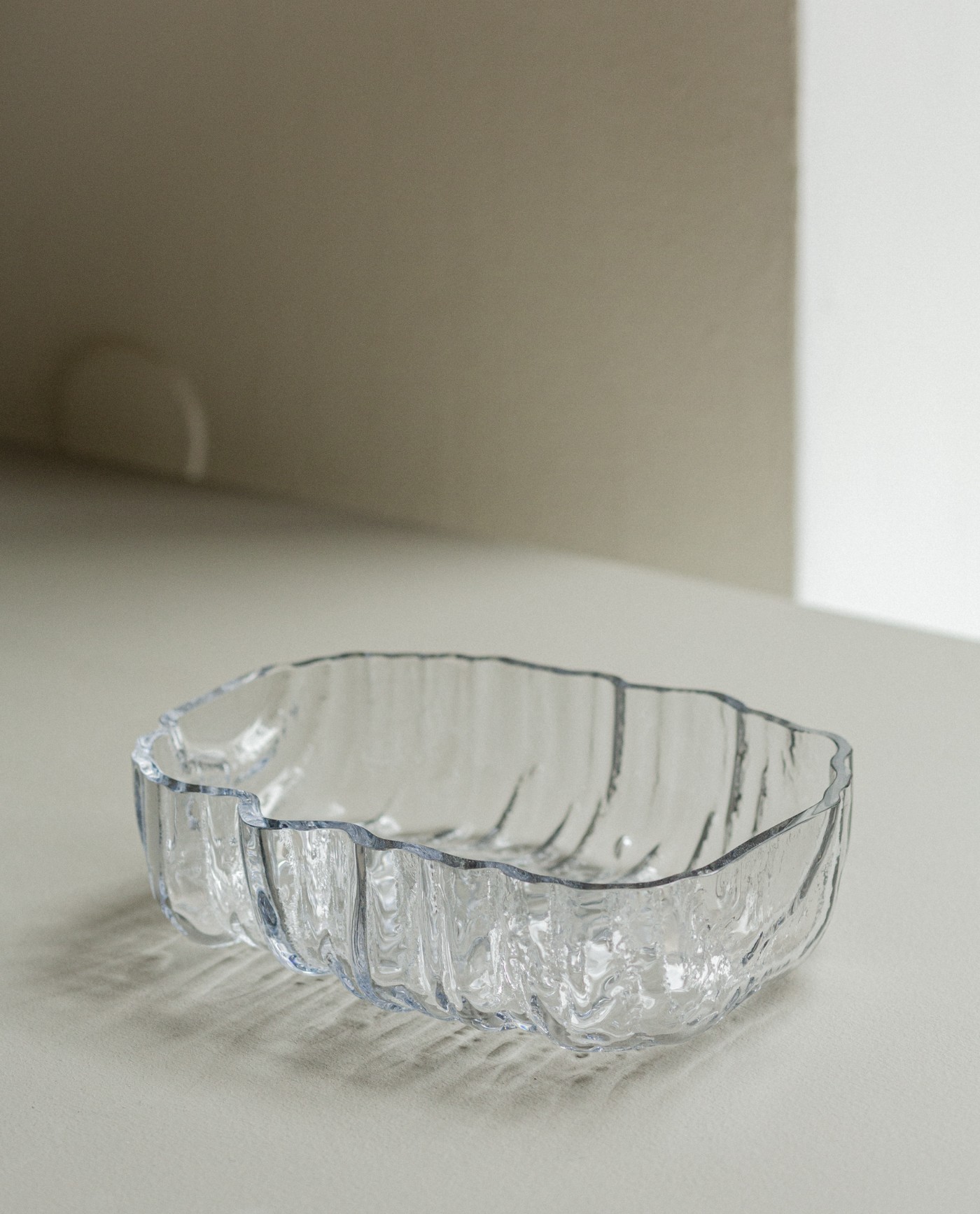 TRACES Exhibition by Antrei Hartikainen — A cast glass vessel with organic, undulating walls sits on a light plaster surface within a minimal interior.