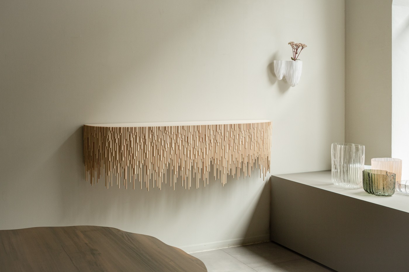 TRACES Exhibition by Antrei Hartikainen — Wall-mounted wooden installation composed of timber slats in graduated lengths suspended from a horizontal rail, creating a cascading fringe that extends...