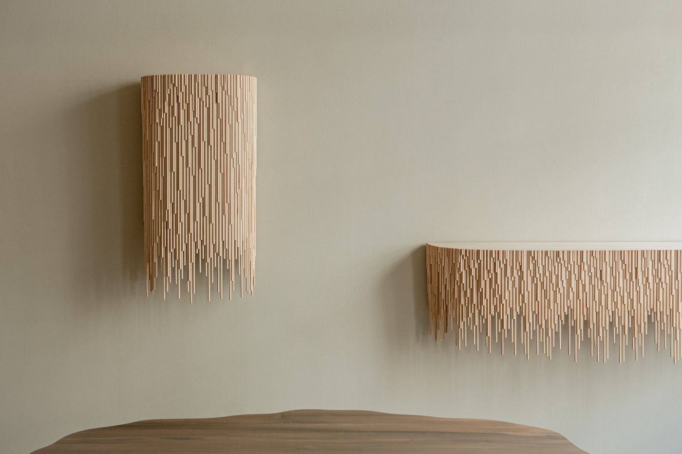 TRACES Exhibition by Antrei Hartikainen — Two wooden wall-mounted installations composed of timber slats suspended from horizontal rails, creating cascading fringe forms of varying lengths.