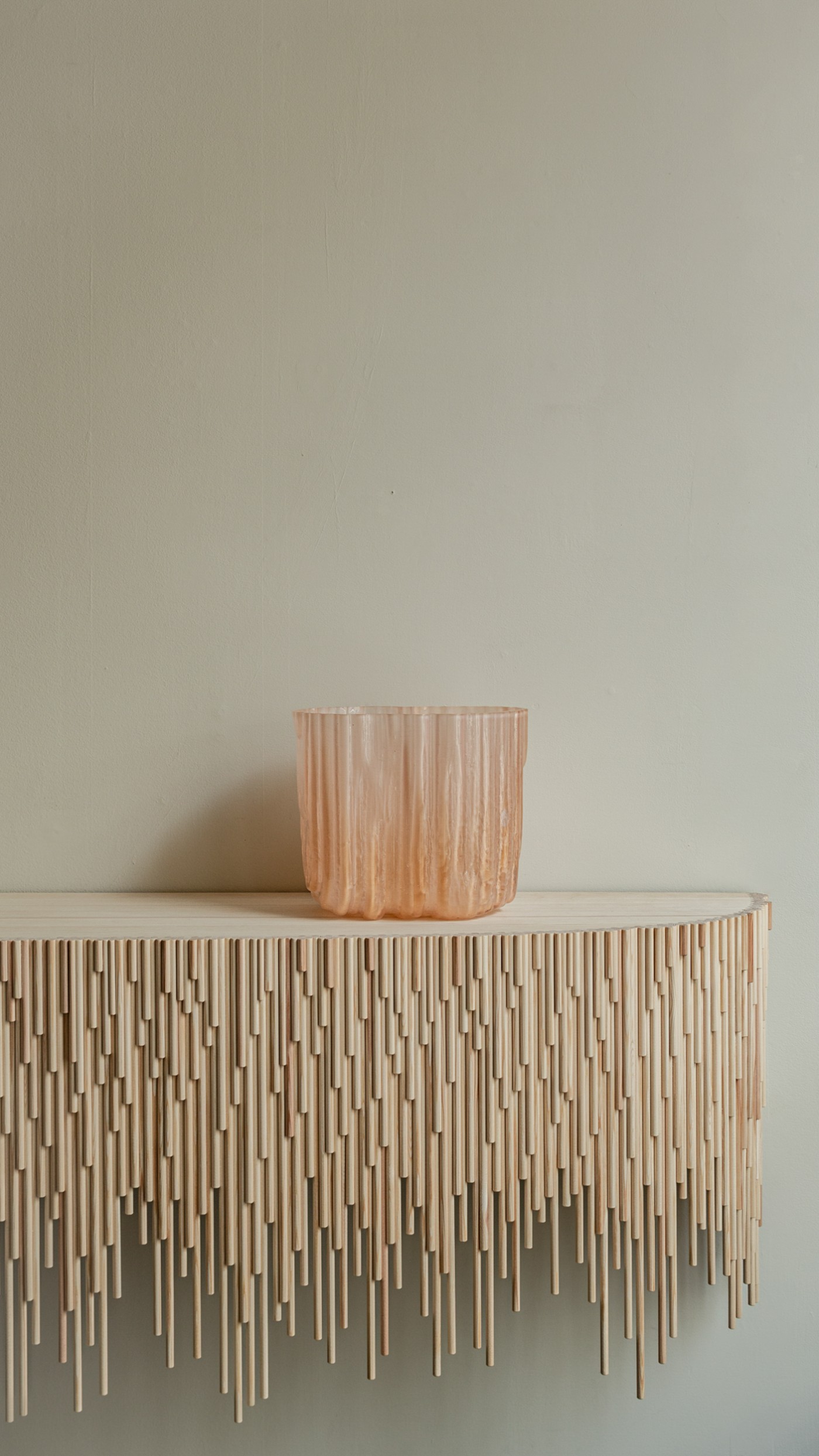TRACES Exhibition by Antrei Hartikainen — A wooden vessel with vertical fluting sits atop a sculptural table composed of suspended timber slats in graduated lengths.