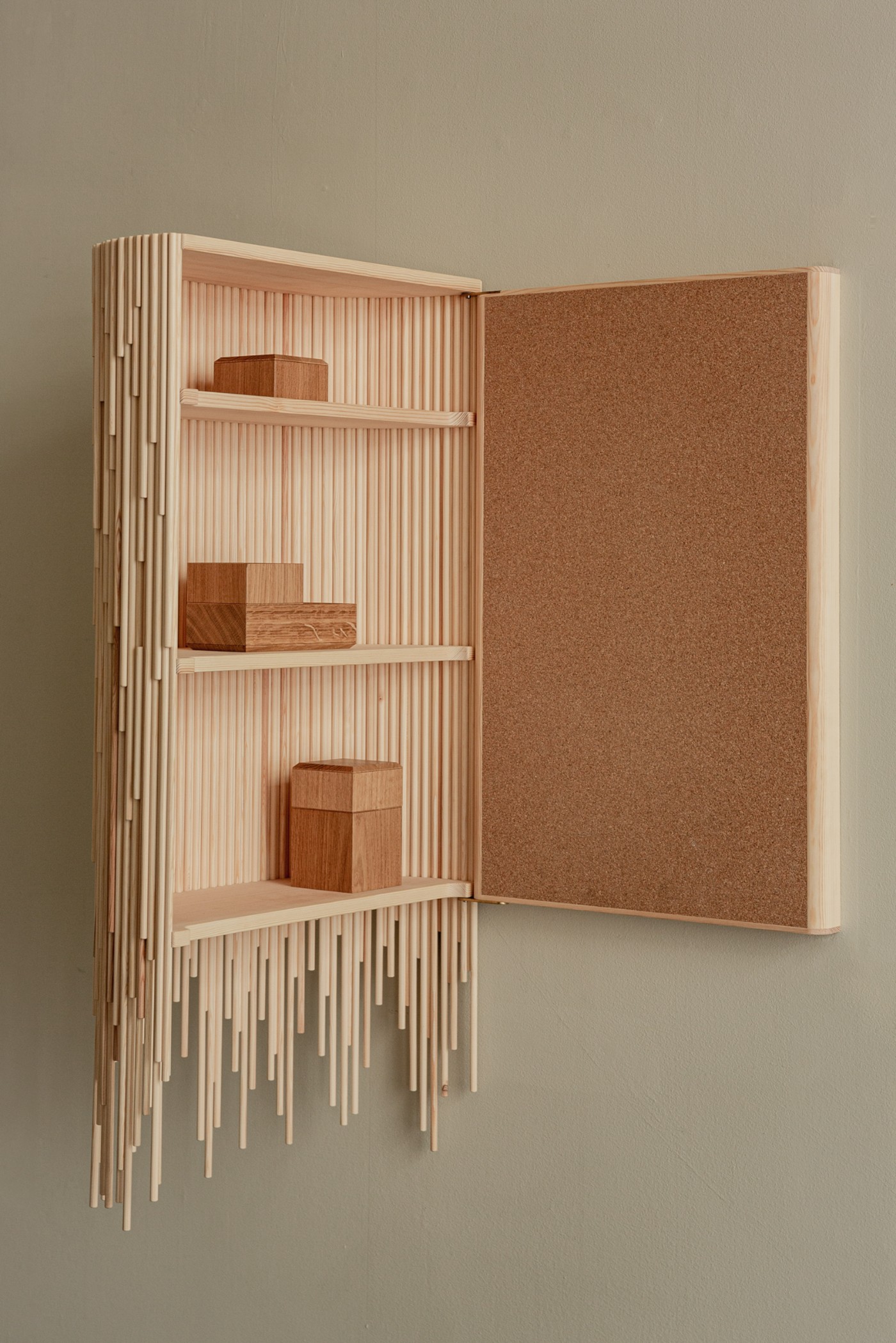 TRACES Exhibition by Antrei Hartikainen — Wall-mounted wooden cabinet with hinged cork-faced door in open position.