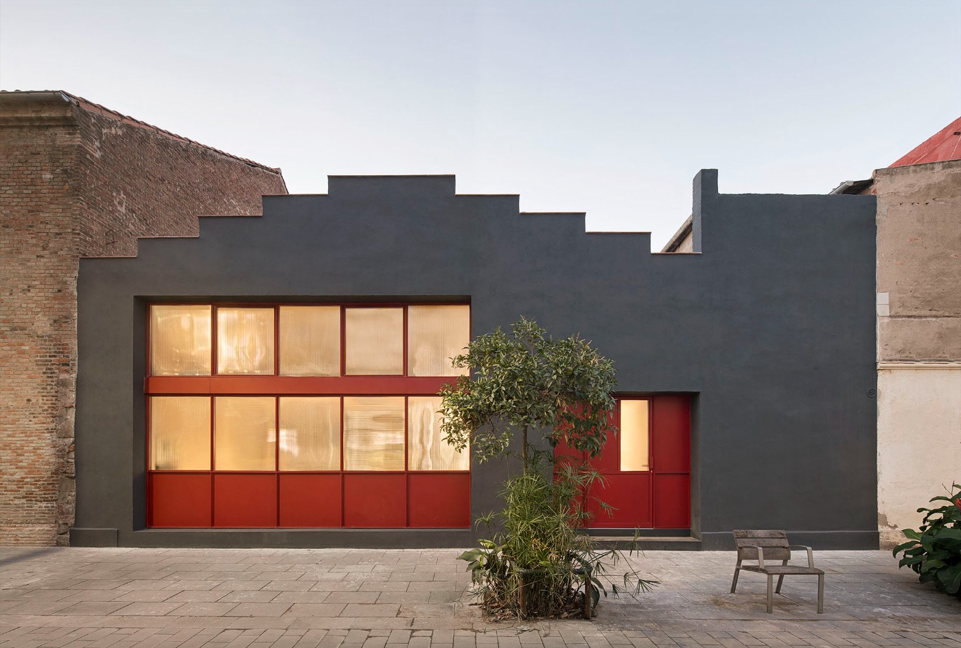 Red House by Aramé Studio — Exterior view of the converted Poblenou factory showcasing the building's primary black-rendered facade with a distinctive stepped parapet profile.