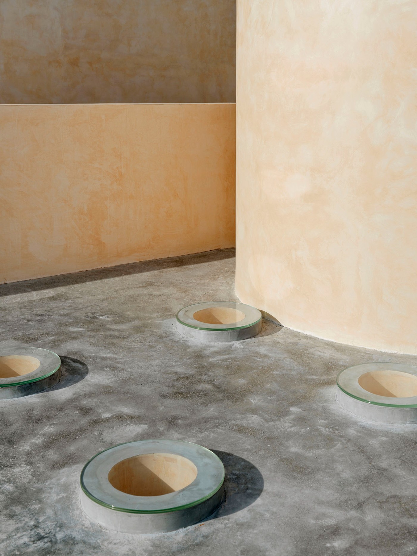 'The Field' by TEAM_BLDG by TEAM BLDG — Four recessed circular apertures punctuate the concrete floor, each topped with a glass ring and revealing ochre-toned cavity walls beneath.