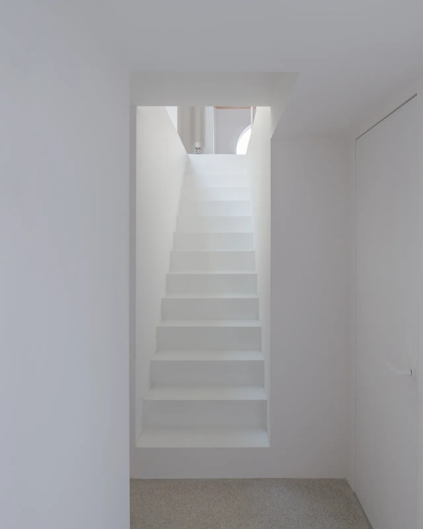 '009_Blue Bird Kitchen' by Studio Tropicana — A monolithic concrete staircase ascends through a whitewashed passage, each tread casting sharp shadows that articulate the vertical sequence.