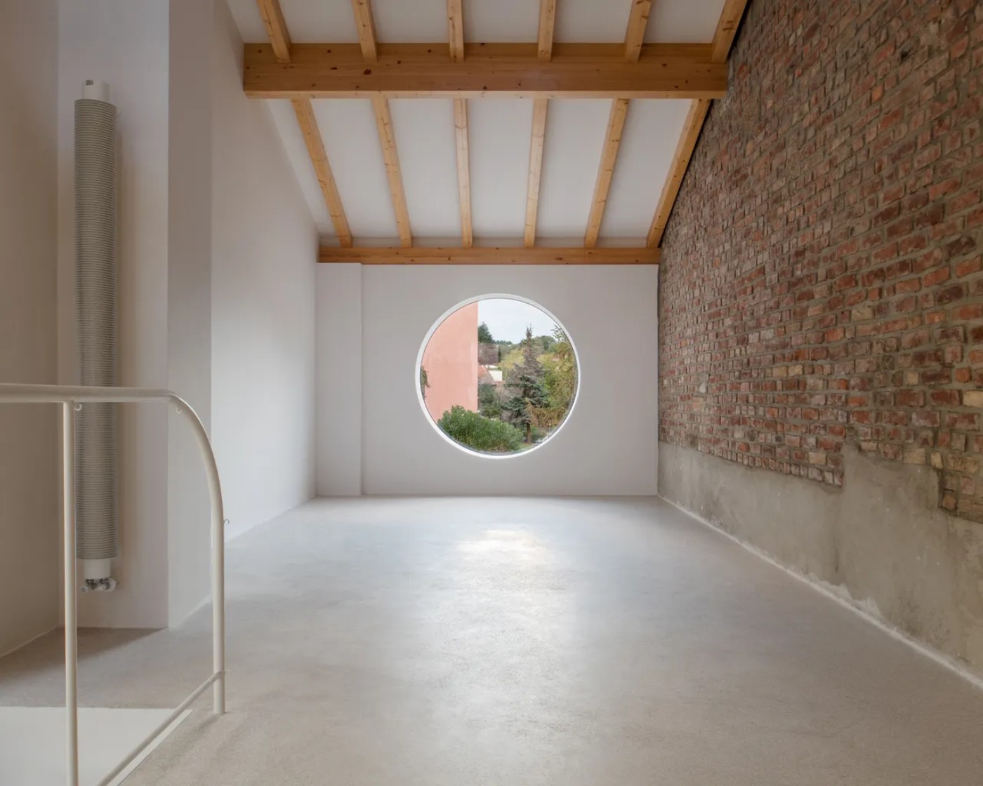 '009_Blue Bird Kitchen' by Studio Tropicana — A double-height interior space illuminates through a circular window punched centrally into the far wall, framing a distant landscape of vegetation and...