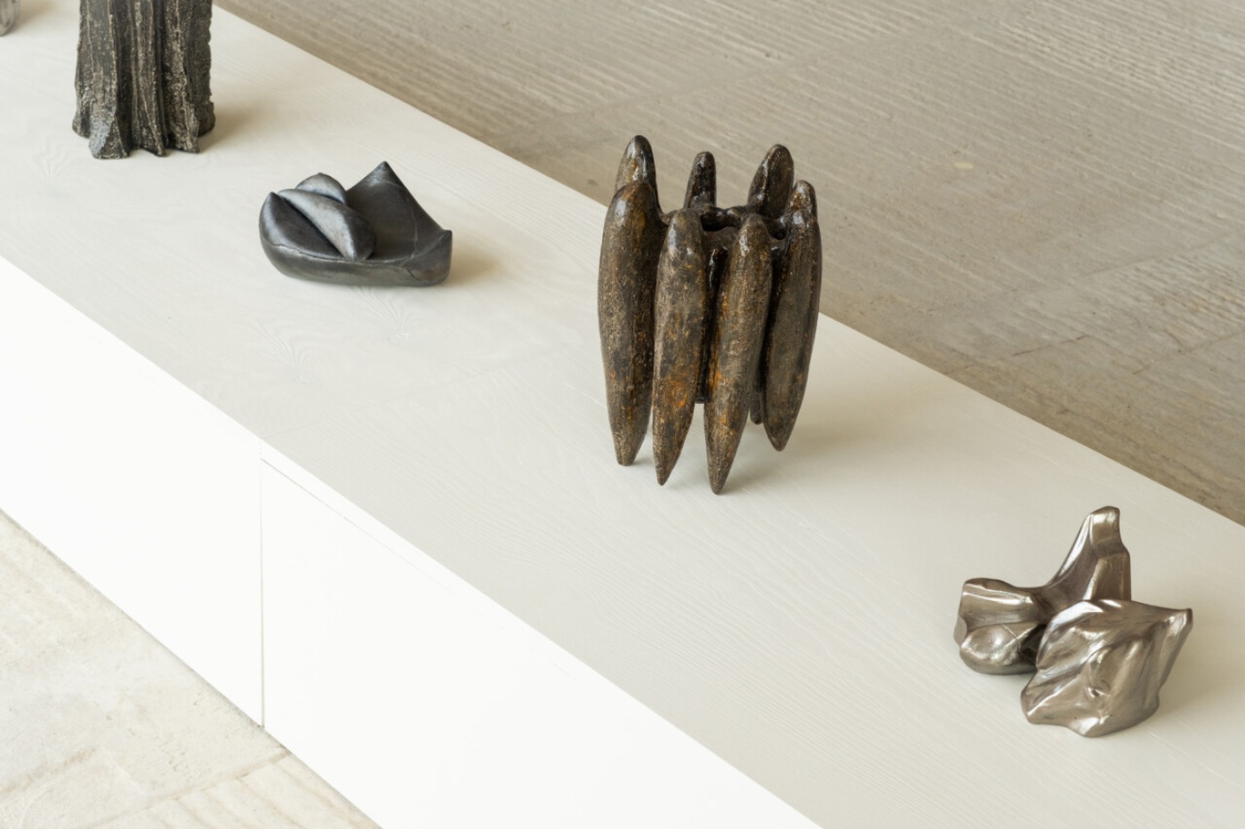 Forma - Nomad Gallery in Berlin by Forma Gallery — A display of cast bronze and patinated metal sculptural objects arranged across a white plaster shelf.