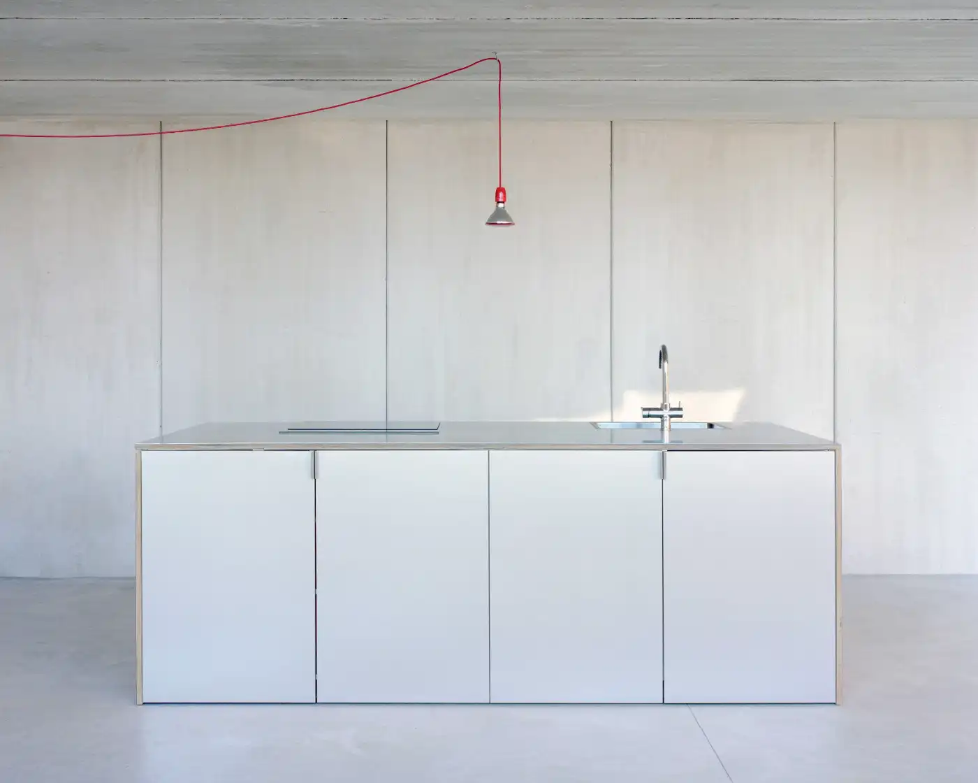 Casa Dosmurs by MESURA — A minimalist kitchen island dominates the frame, its white lacquered cabinetry punctuated by vertical stainless steel handle pulls.