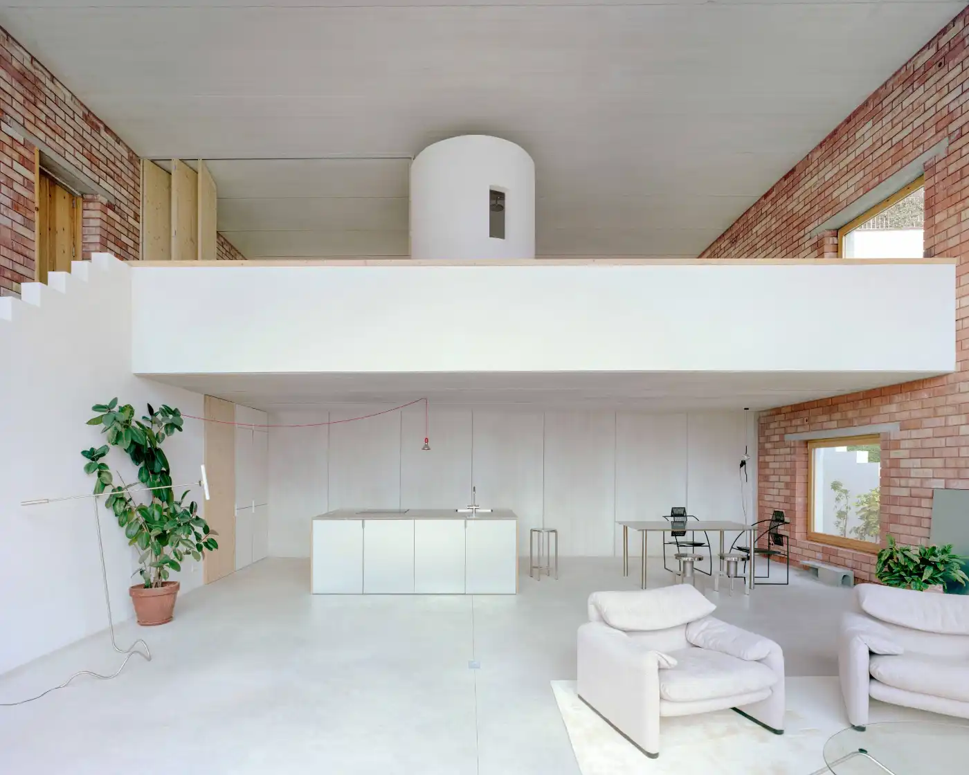 Casa Dosmurs by MESURA — Interior view of Casa Dosmurs revealing a double-height loft space with exposed brick parapet walls framing the upper level.