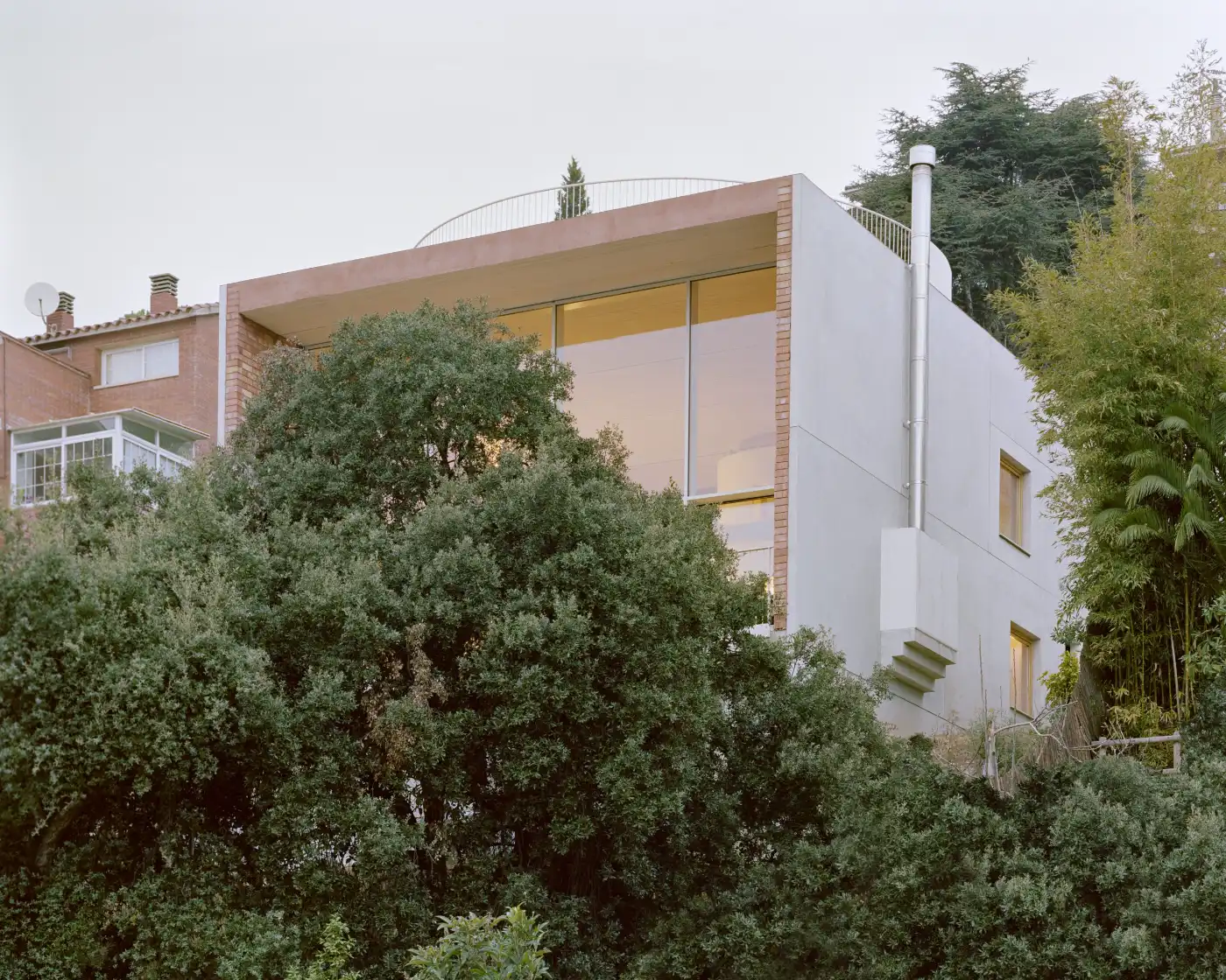 Casa Dosmurs by MESURA — Casa Dosmurs presents itself as a white rendered volume with selective transparency, its upper facade dominated by a horizontal bronze-framed glazing band...