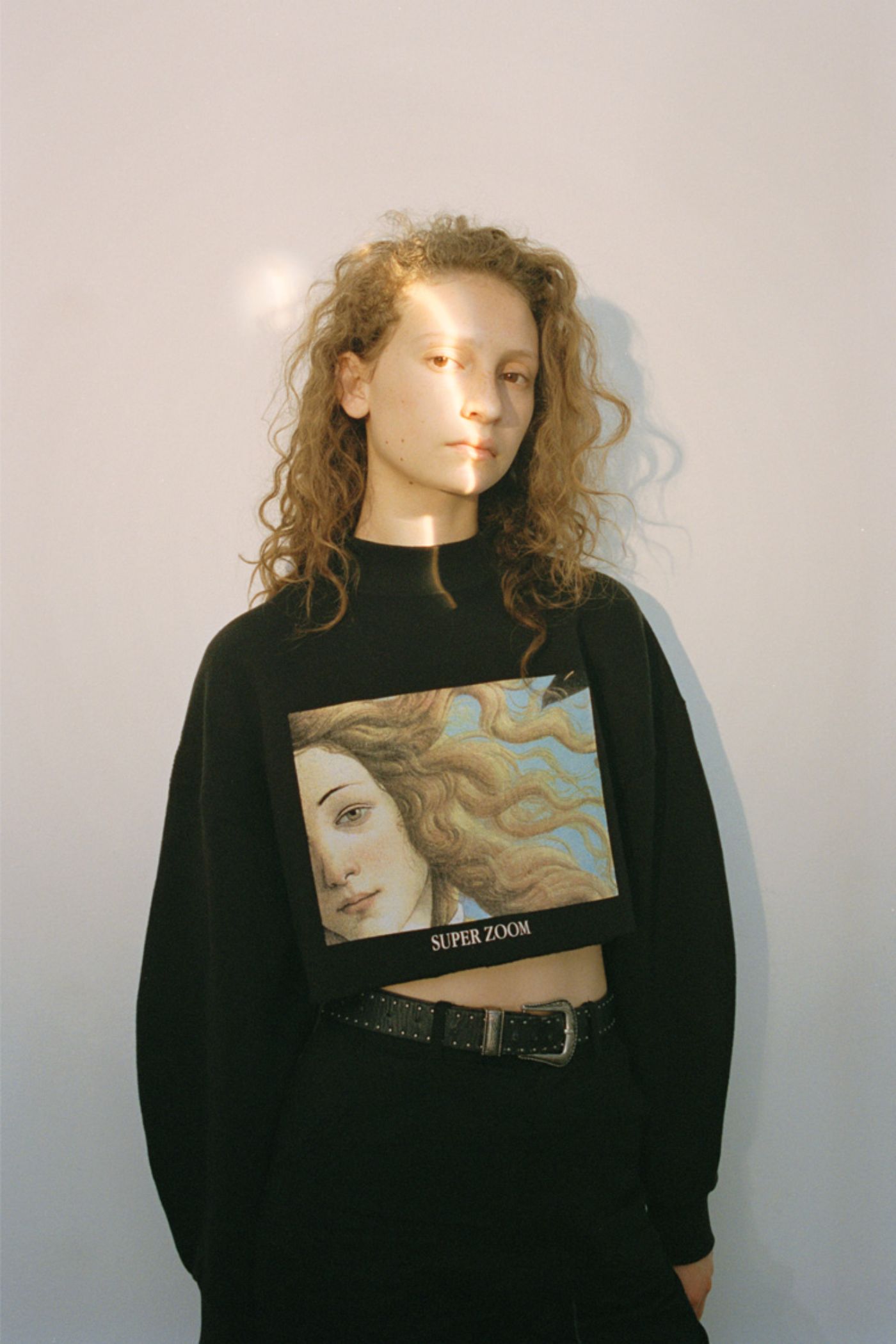 Visitors+ by Piczo — Cropped portrait of a young subject in black long-sleeve sweatshirt with graphic print featuring Renaissance-style portrait and 'SUPER ZOOM' text.