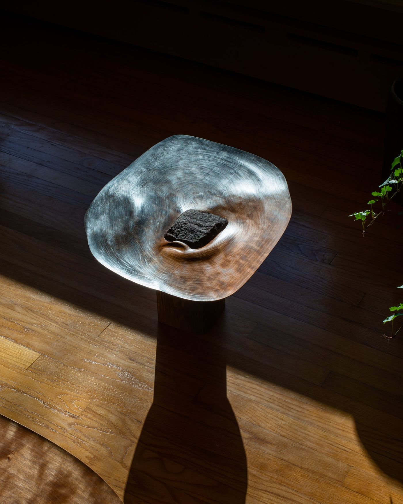 Selected 'Kanna' works by Studiovoll — A sculptural wooden vessel mounted on a dark cylindrical base occupies the center of a wood-floored interior.