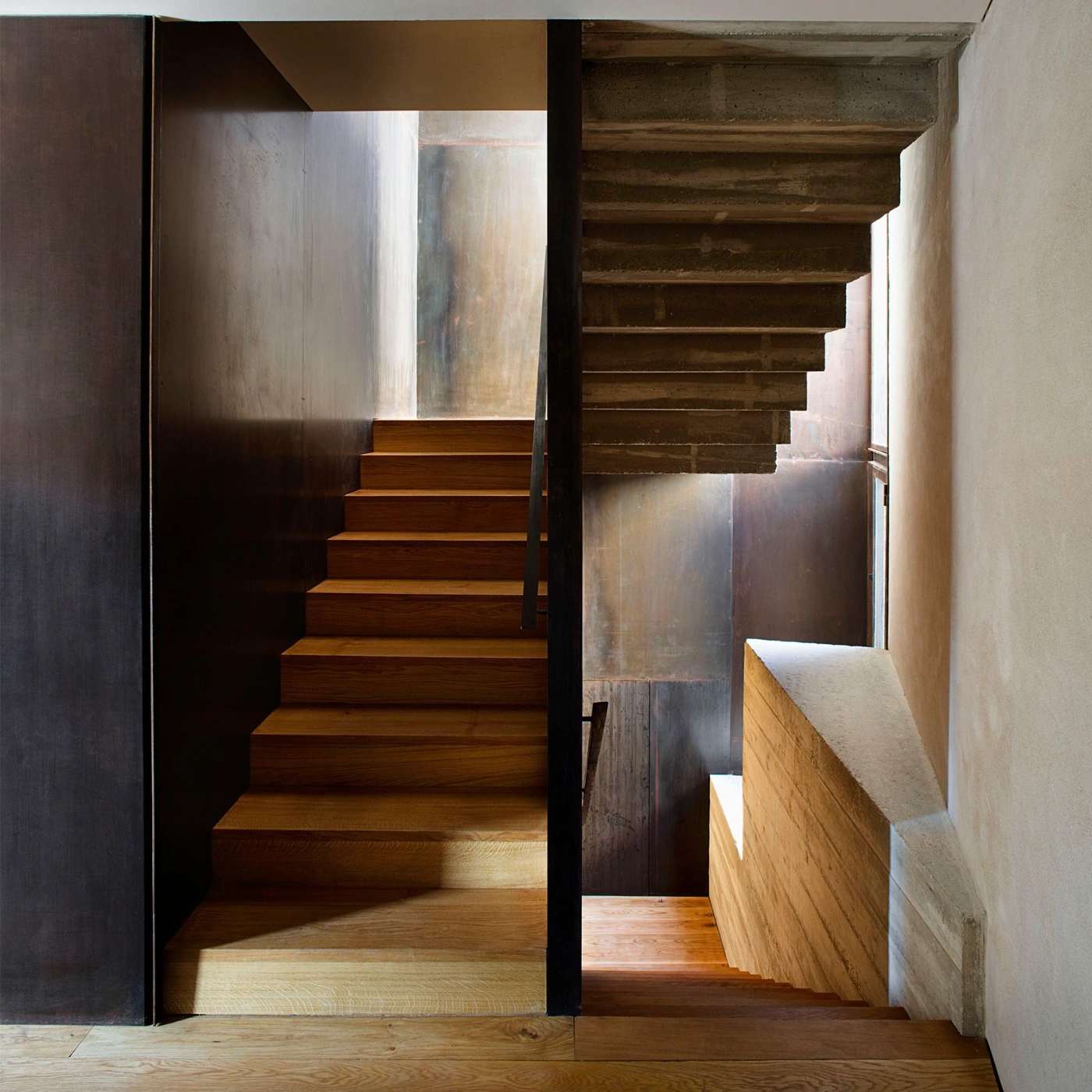 Alemenys 5 by Anna Noguera — A dual staircase composition divides the frame into two ascending timber flights separated by a charcoal-toned timber partition wall.