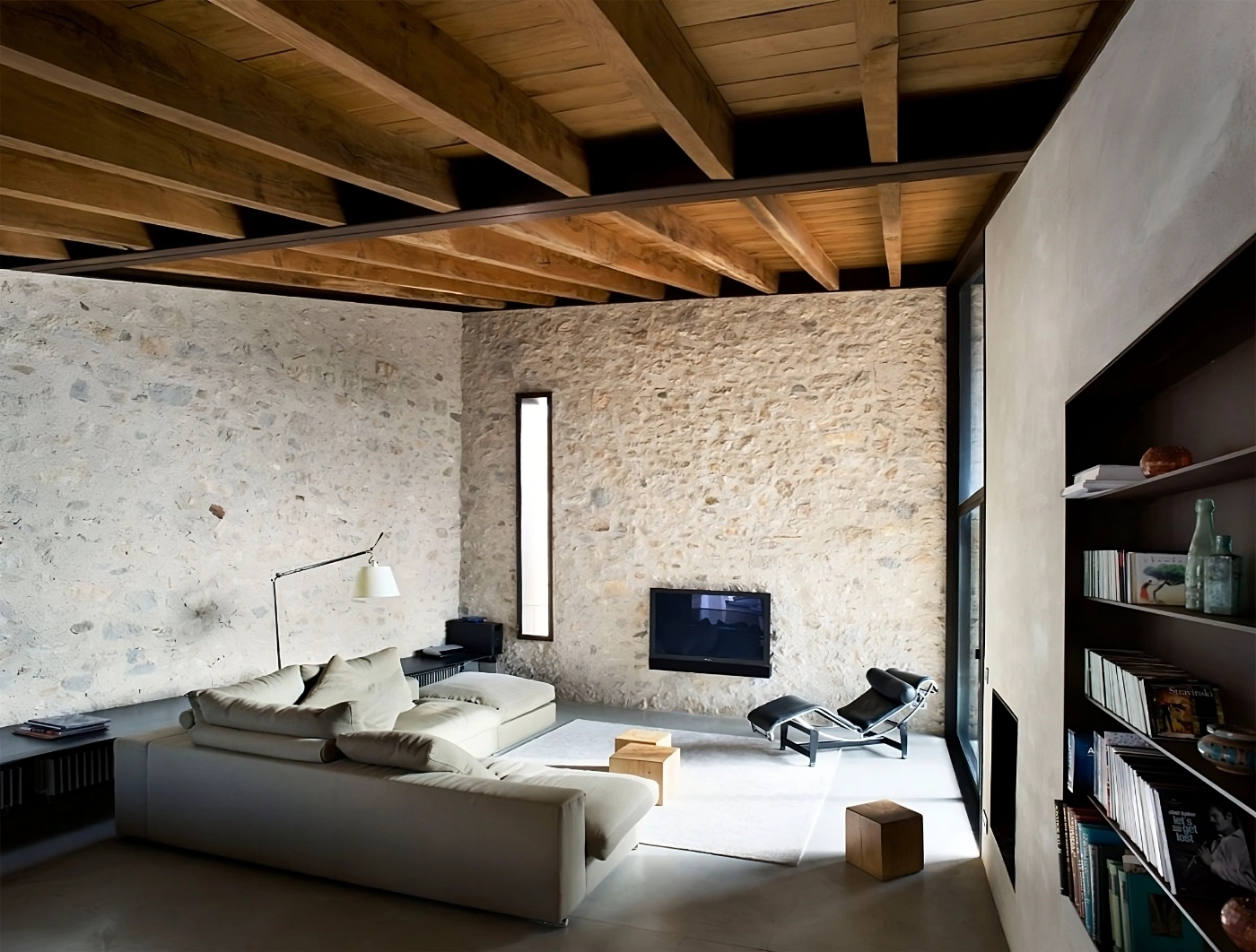 Alemenys 5 by Anna Noguera — A minimalist living space defined by massive rammed-earth walls in cream and ochre tones, punctuated by a vertical slot window admitting a narrow column of...