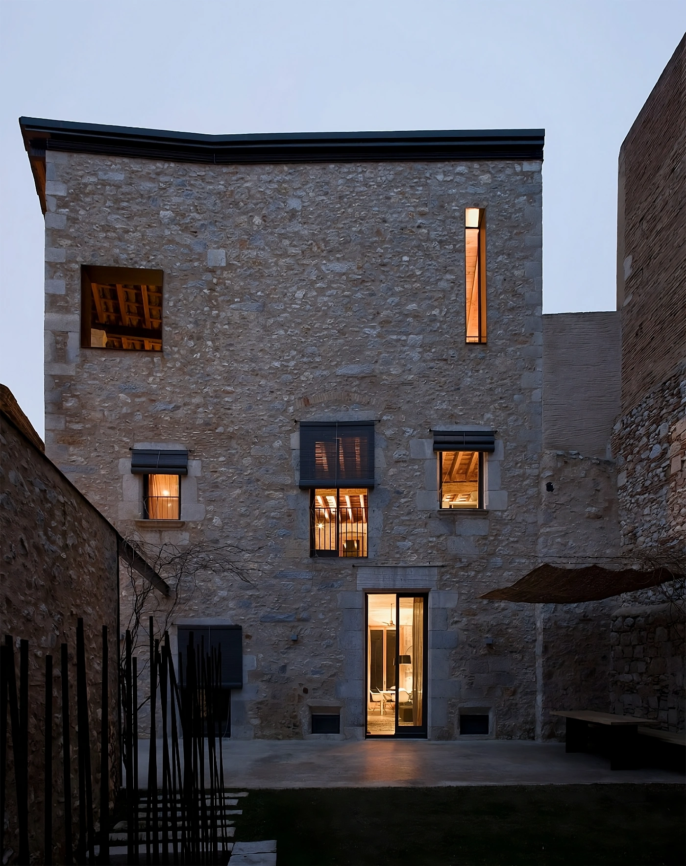 Alemenys 5 by Anna Noguera — Evening photograph of a restored medieval stone tower in Girona's old quarter, captured from the narrow courtyard at dusk.