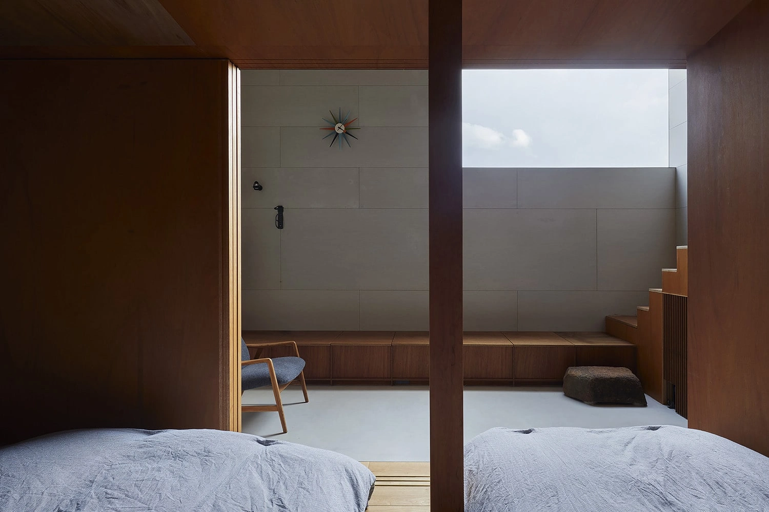 House in Gamo by Suppose Design Studio — A view from the bedroom into an adjoining timber-lined space, separated by dark timber structural columns.