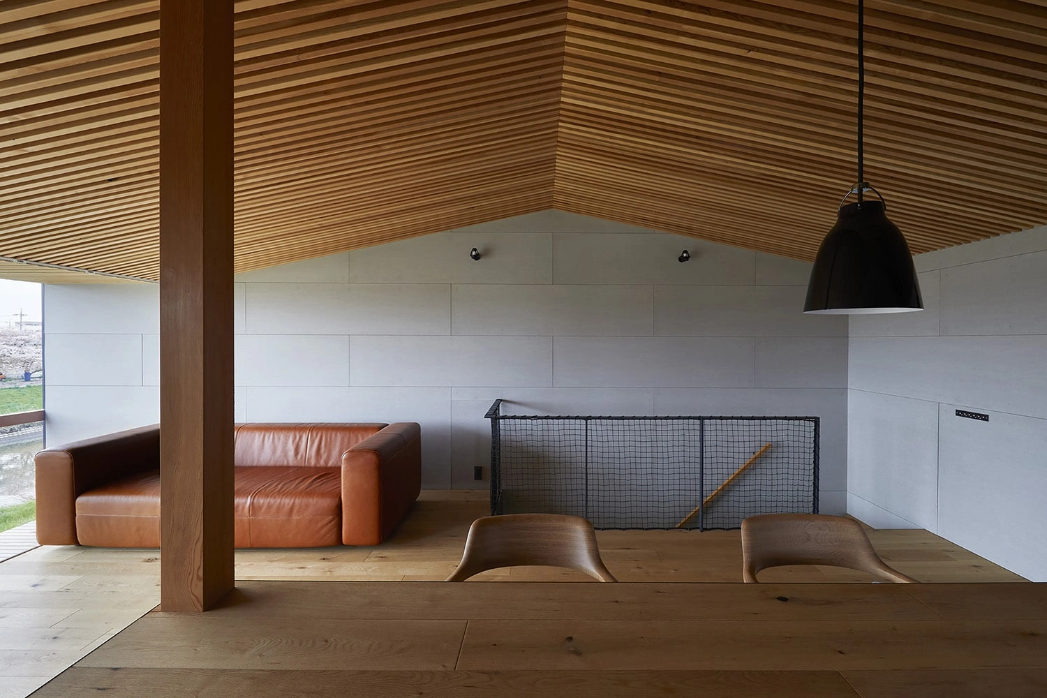 House in Gamo by Suppose Design Studio — Interior view of the open-plan living space reveals a post-and-beam structural system with a prominent timber column anchoring the composition.
