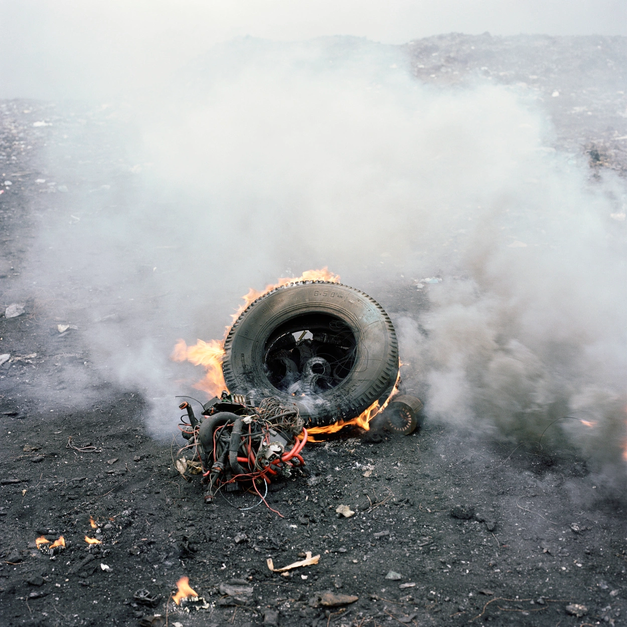 Permanent Error by Pieter Hugo — A burning tire engulfed in white smoke dominates the composition, its rubber charred orange and black at the edges.