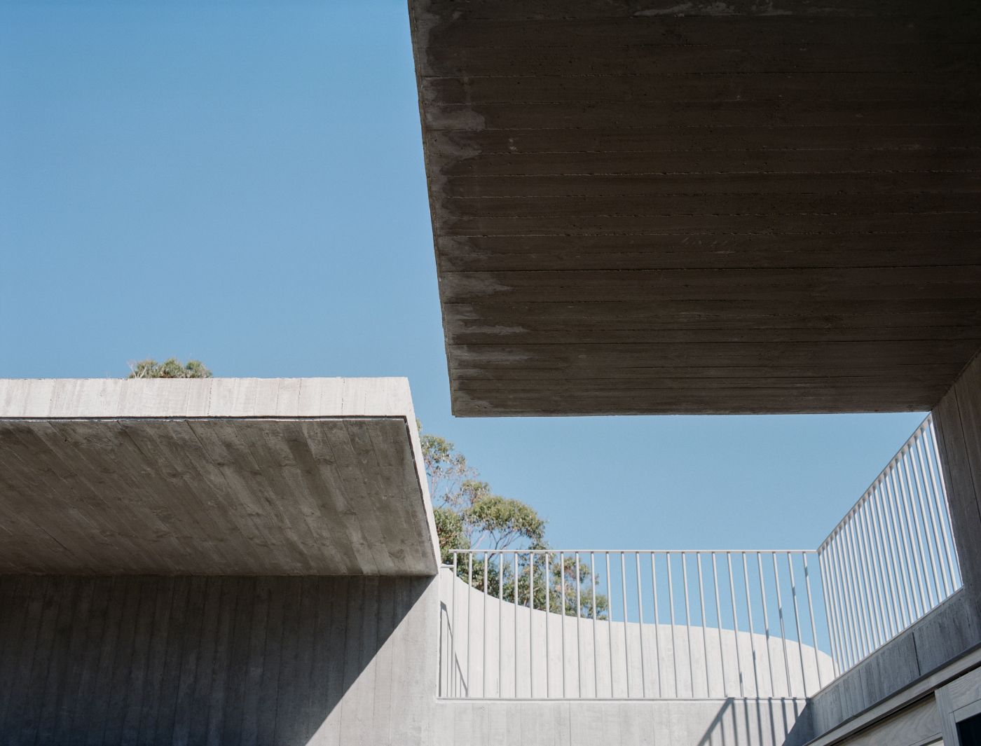 Mori House by Aires Mateus + MAArchitects — View from within a courtyard defined by monolithic concrete walls and steel-railed balconies.