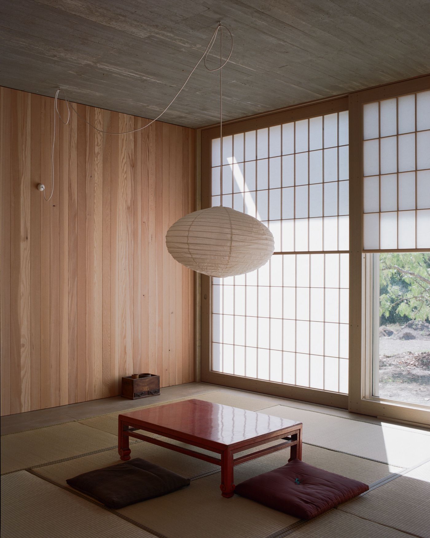 Mori House by Aires Mateus + MAArchitects — A Japanese-inflected interior anchored by a low red-lacquered table positioned on the woven tatami mat floor.