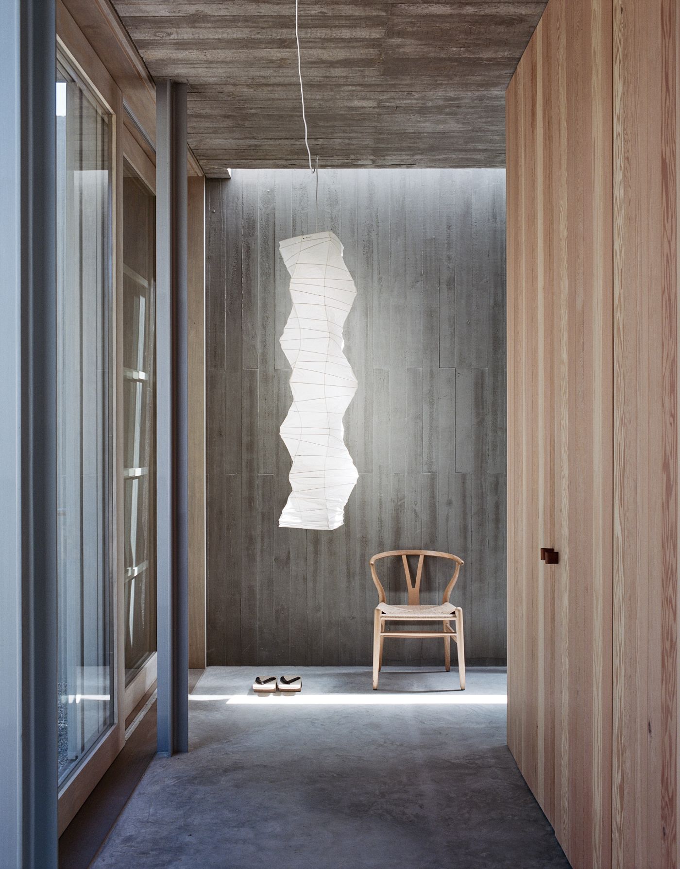 Mori House by Aires Mateus + MAArchitects — A passage frames a bedroom alcove with whitewashed vertical timber wall paneling and polished concrete flooring.
