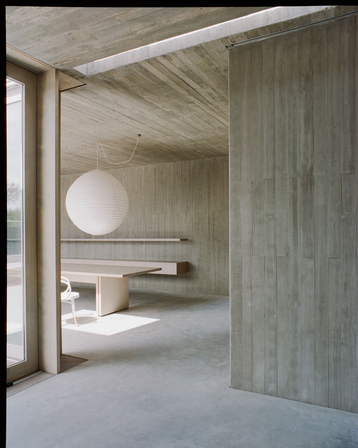 Mori House by Aires Mateus + MAArchitects — A threshold view into a concrete-floored interior defined by board-formed concrete walls and ceiling.