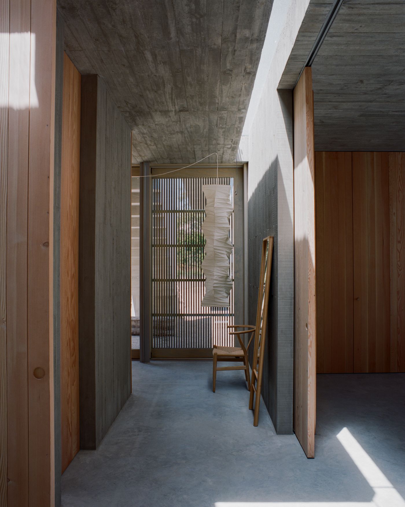 Mori House by Aires Mateus + MAArchitects — A narrow passage frames a mid-century leather armchair positioned against a vertical timber-paneled wall.